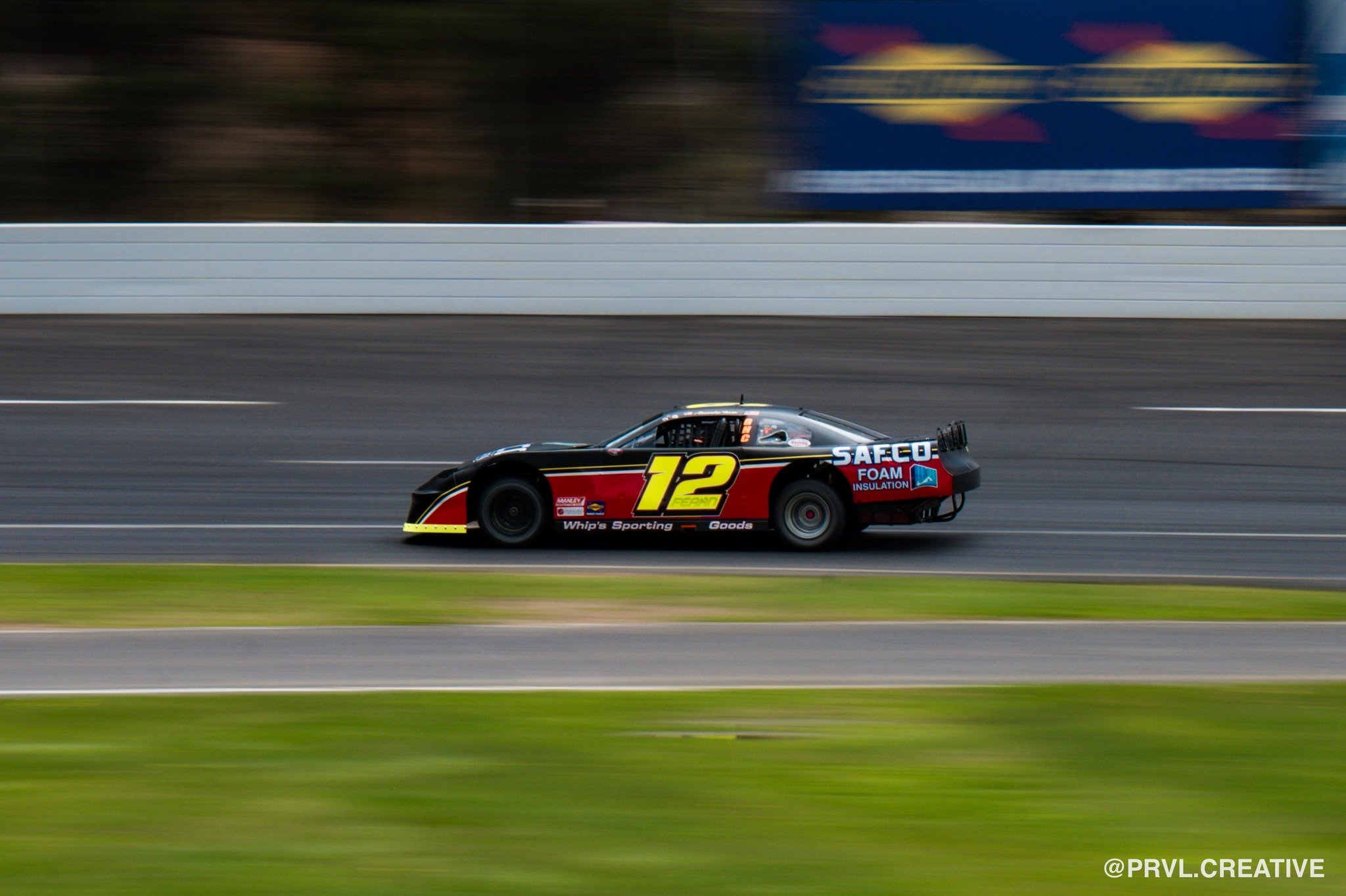 A black racing car with the number 12 on its side, speeding along a race track with motion blur.
