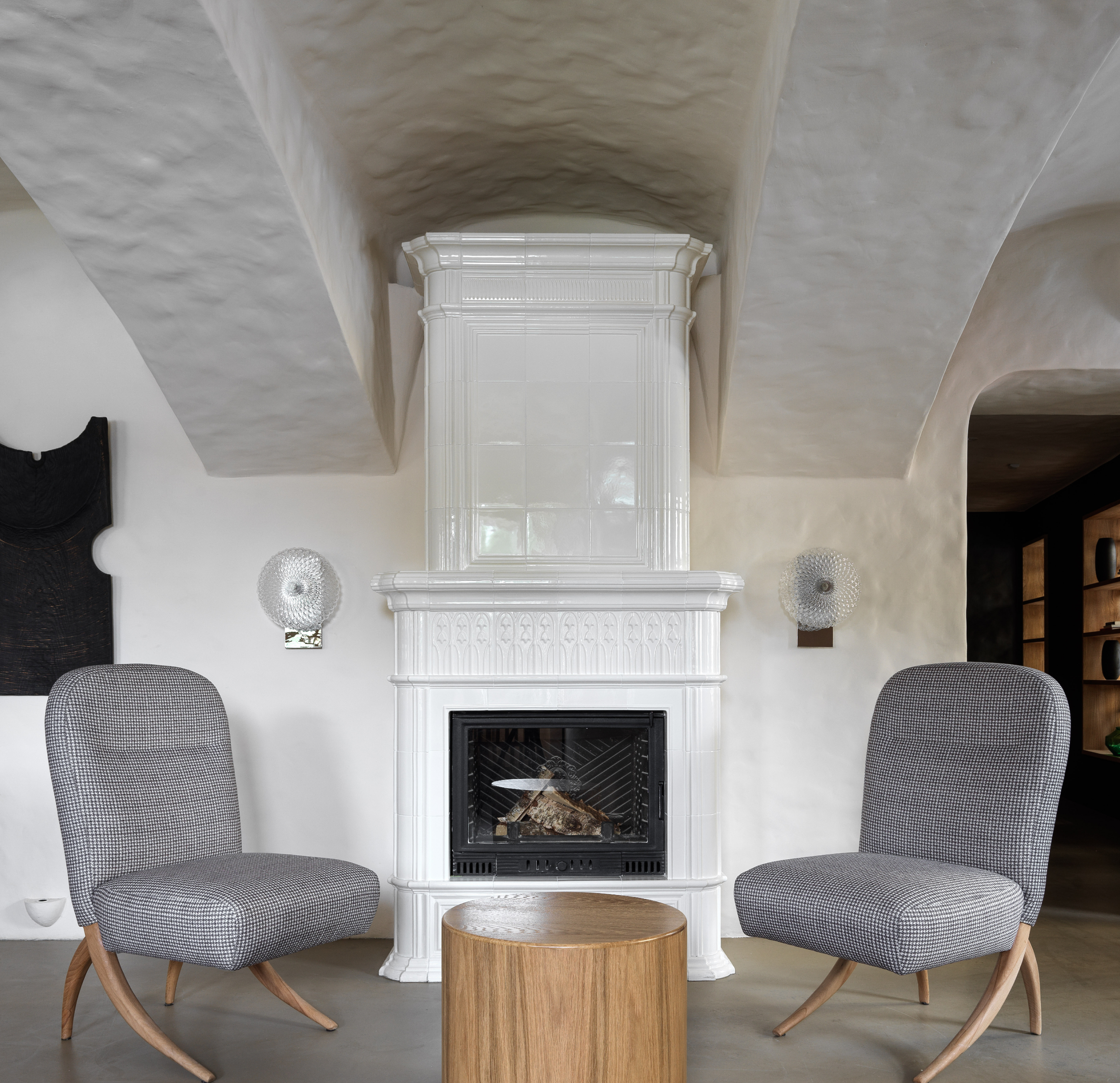 Contemporary interior with a white fireplace, two gray upholstered chairs, and a round wooden table.