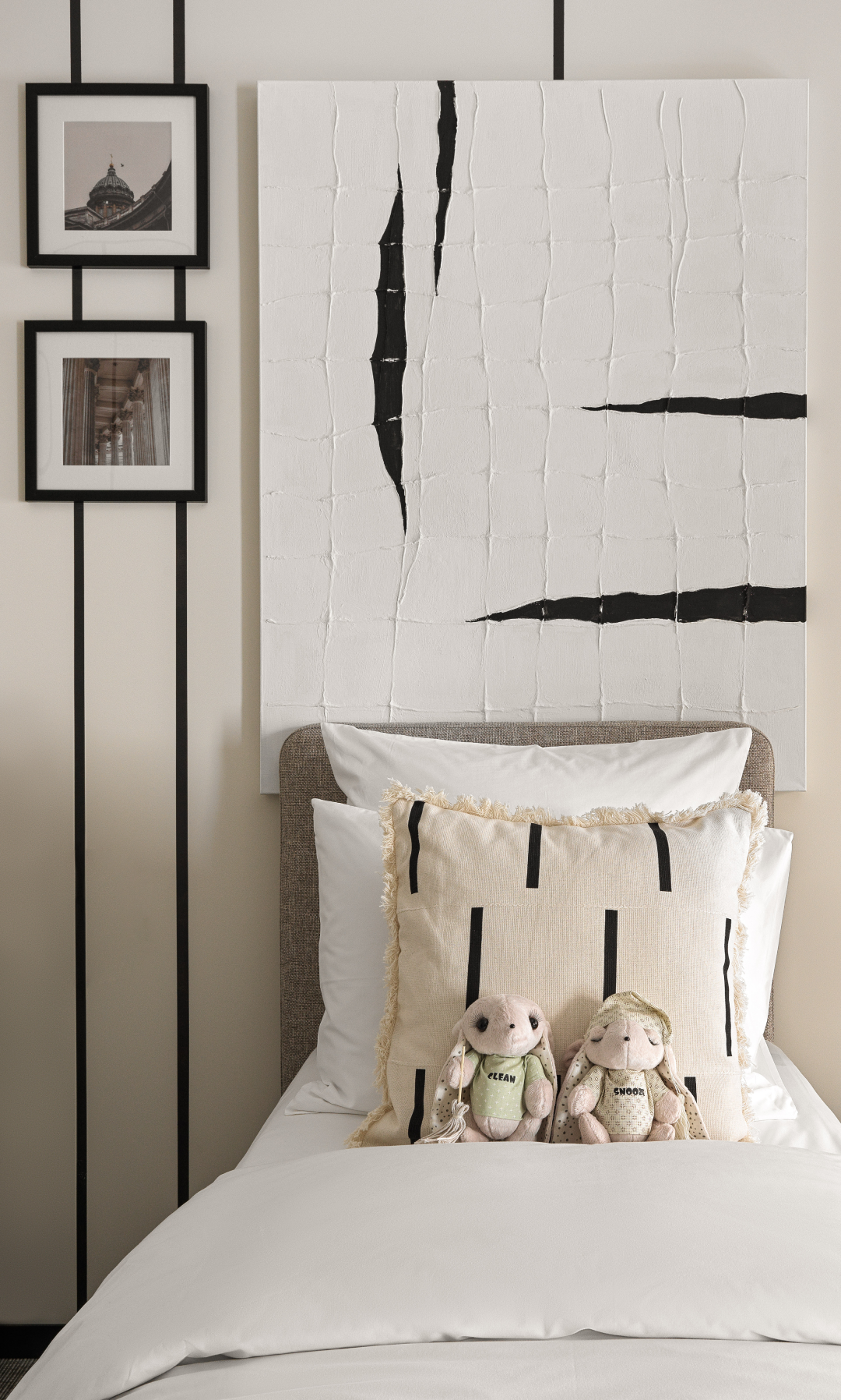 Bedroom with white bedding, decorative pillows, two plush bunny toys, black and white abstract wall art, and framed photographs.