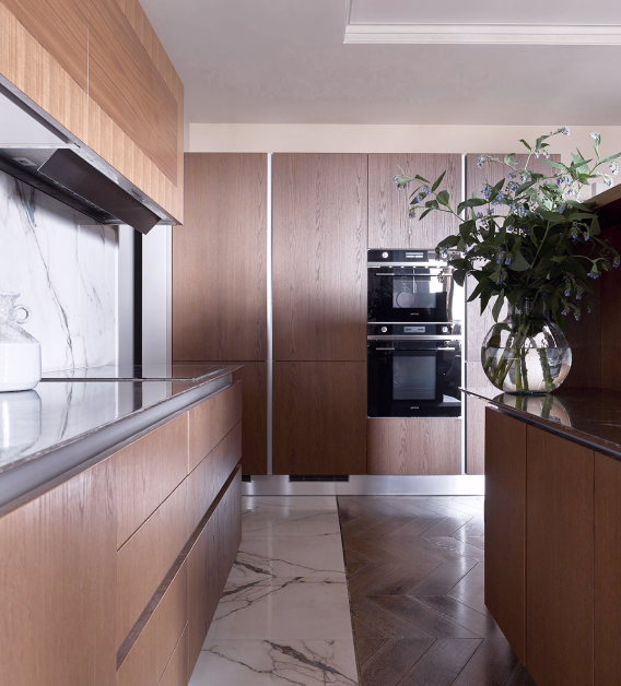 Modern kitchen with wooden cabinets, marble backsplash and floor, built-in ovens, and a vase of flowers on the countertop.