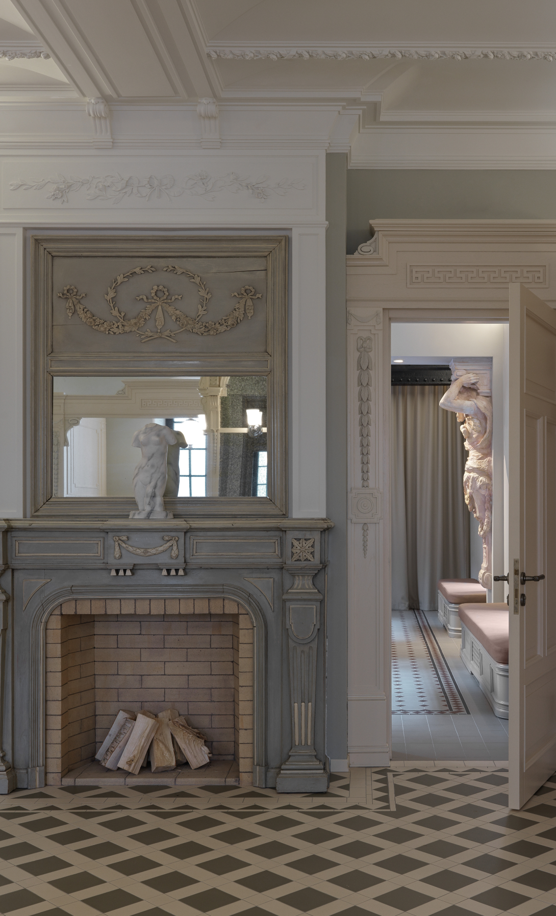Elegant interior with a traditional fireplace, decorative molding, and a sculpture in an adjacent room visible through an open door.