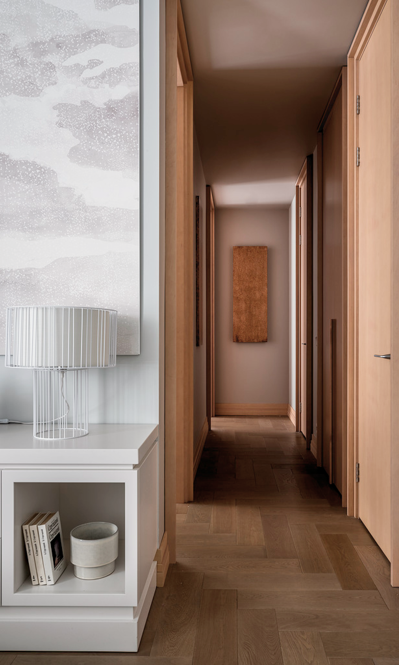 Minimalist hallway with wooden flooring, a side table featuring a wire-framed lamp and books, and a framed artwork on the wall.