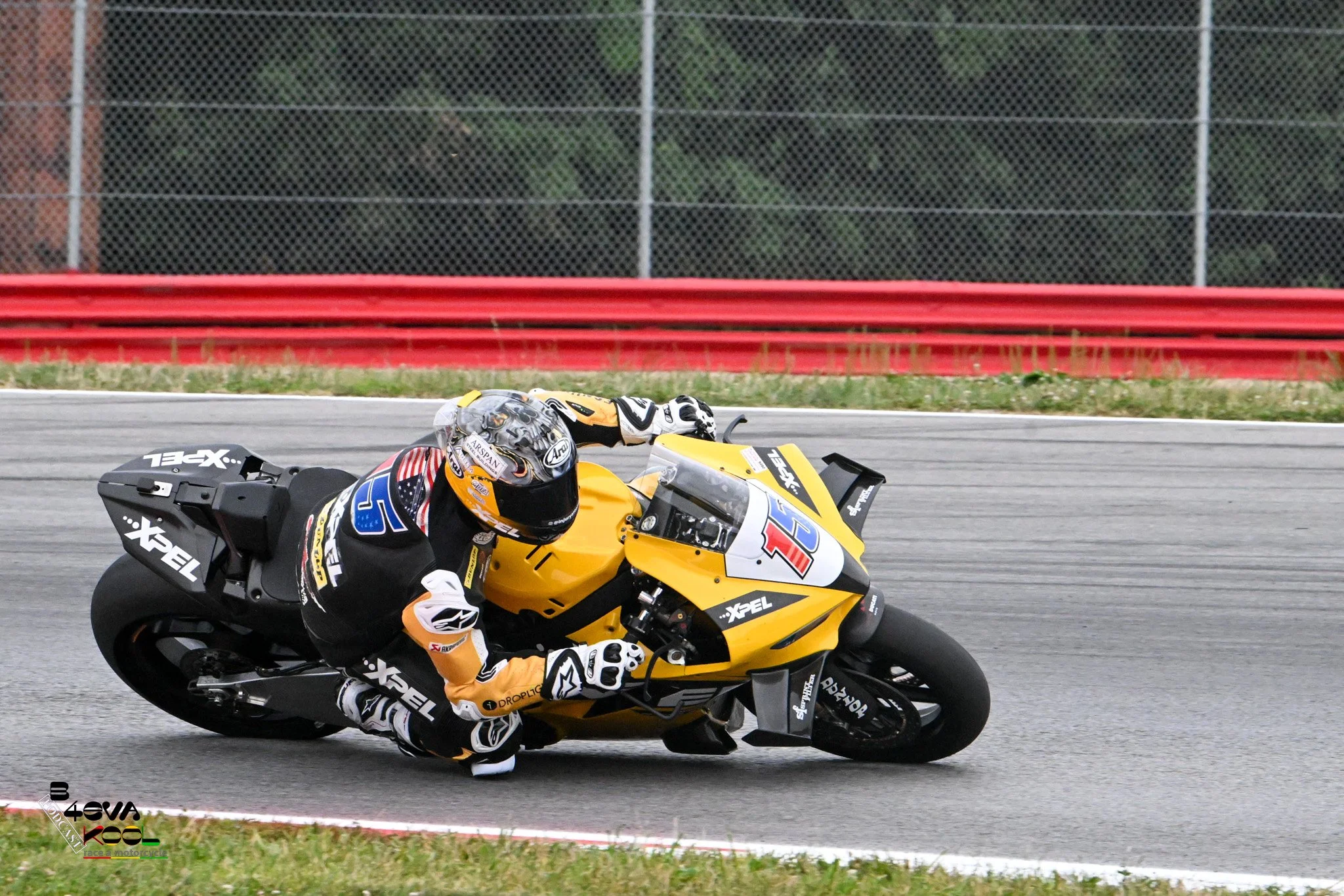 Motorcycle racer in black and yellow suit leaning into a turn on a race track with a yellow race bike, helmet, and racing gear.