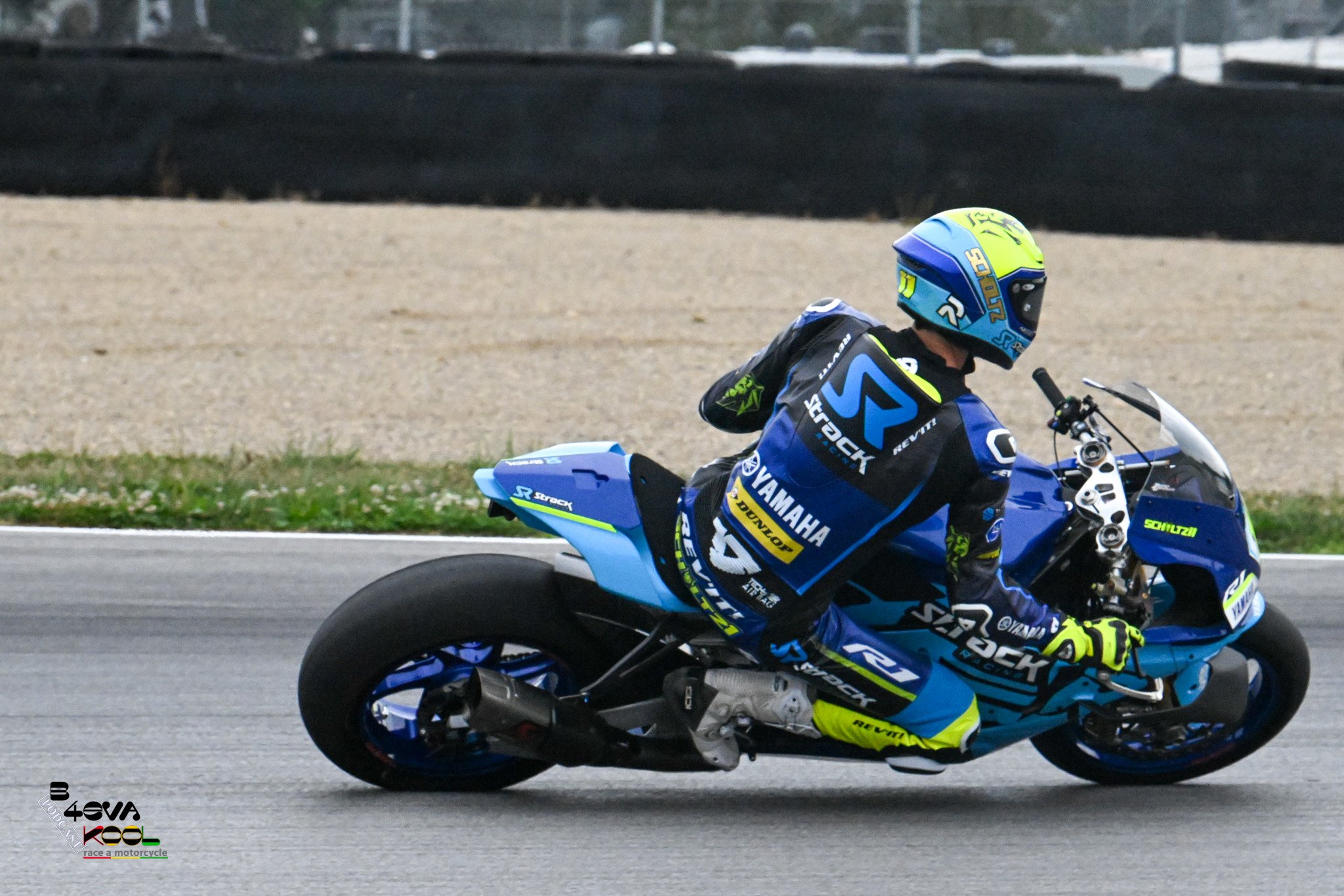 A motorcyclist dressed in blue and yellow racing gear leaning into a turn on a blue sport motorcycle on a paved road.