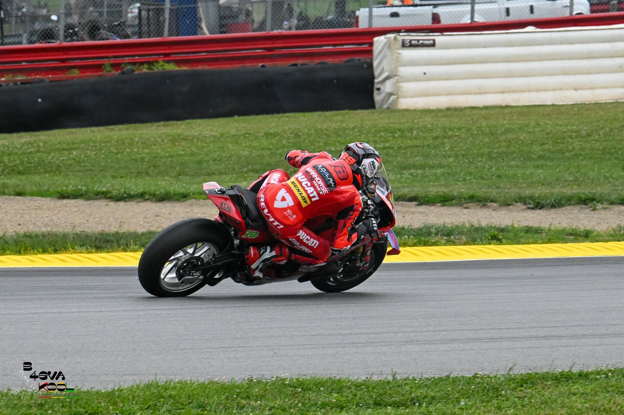 Motorcycle racer in red racing suit leaning into a turn on a race track.