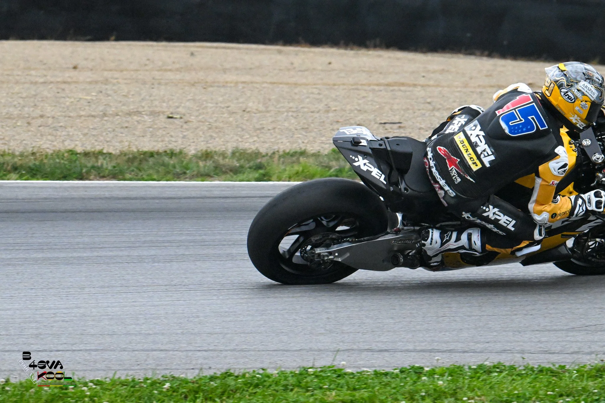 Motorcycle racer in black and yellow gear leaning into a turn on the racetrack.