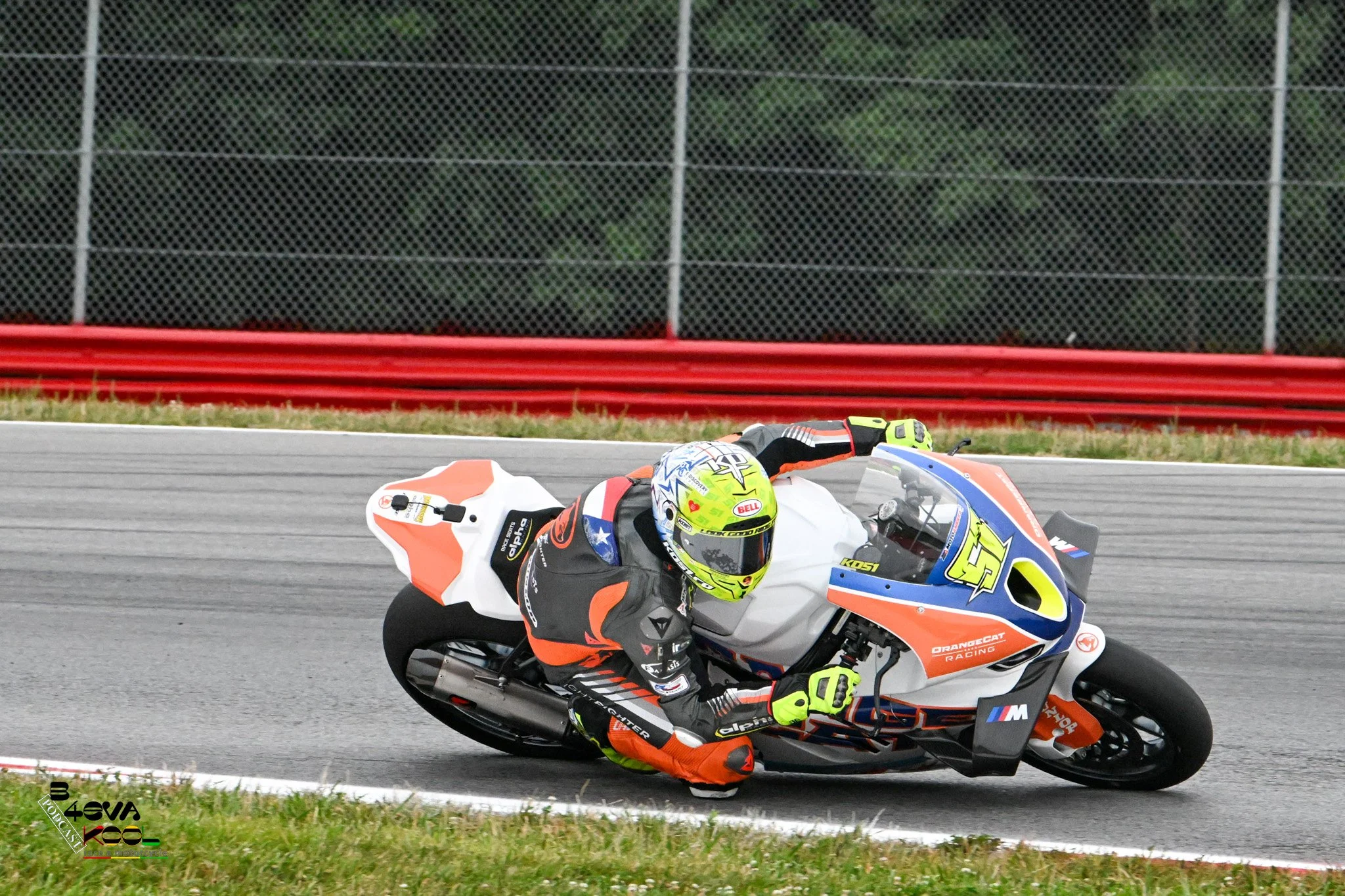 A motorcycle racer in a neon yellow helmet and racing suit leaning into a turn on a race track.
