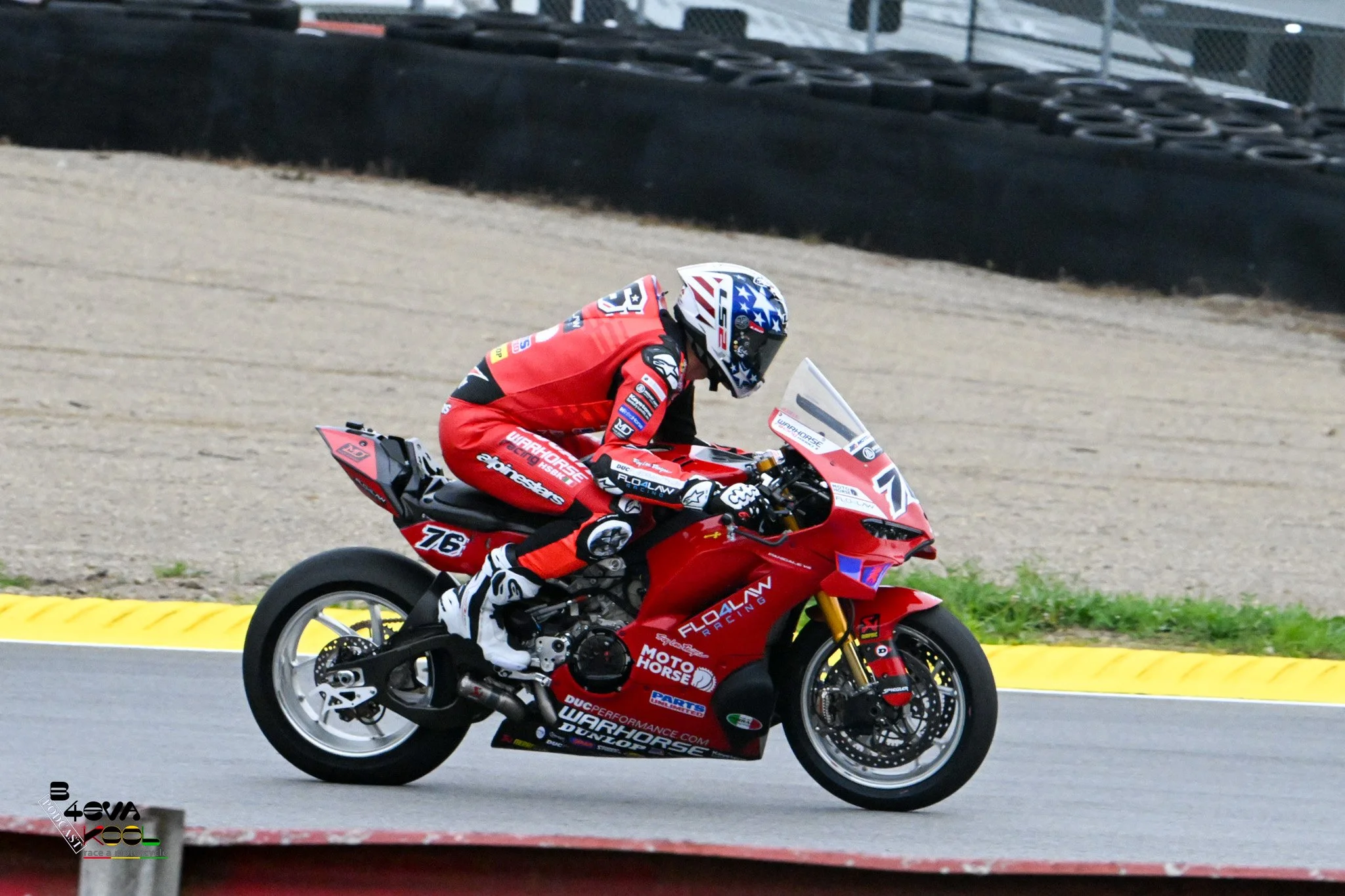 A person riding a red motorcycle on a racetrack, wearing a red racing suit and a helmet with stars and stripes design.