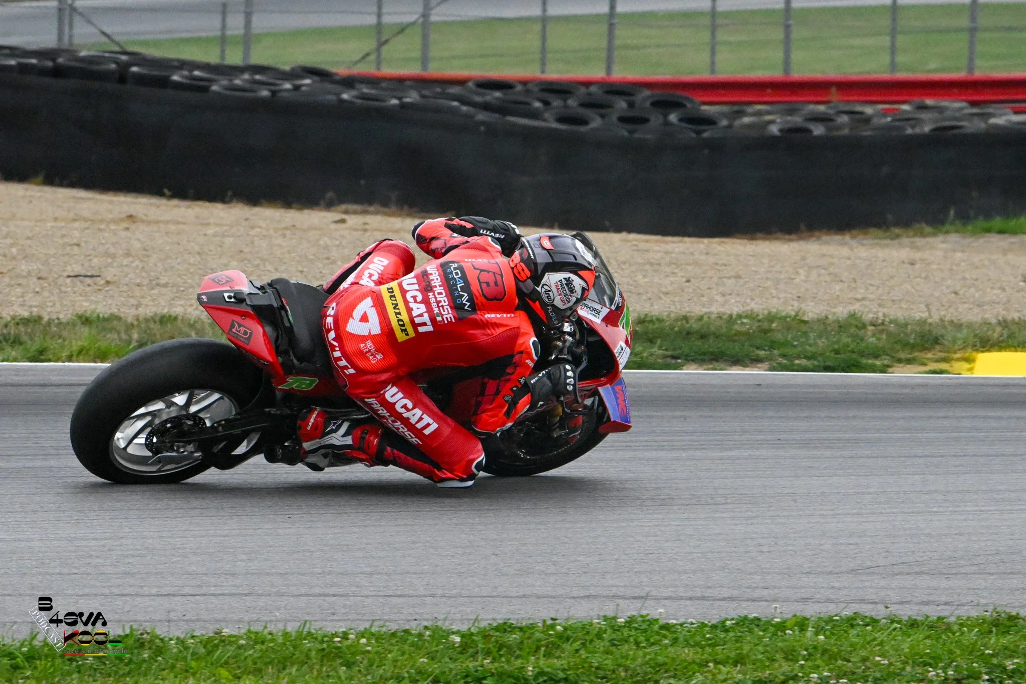 Motorcycle racer in red racing suit leaning into a turn on a racetrack.