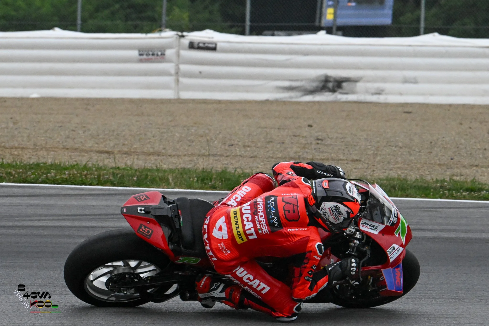 A professional motorcycle racer in red gear leaning sharply into a turn on a racetrack.