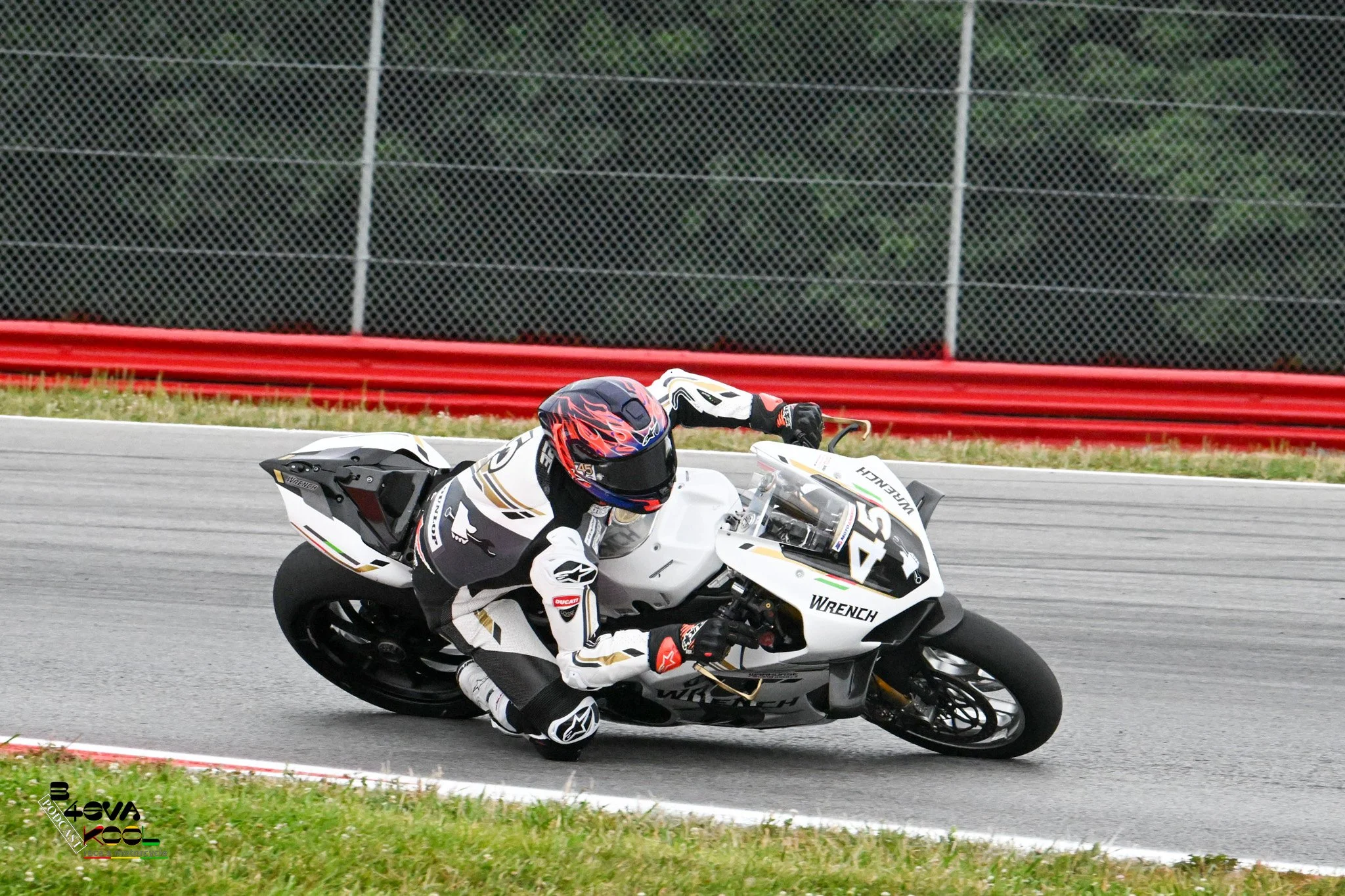 Motorcycle racer wearing a white racing suit and helmet, leaning into a turn on a racetrack.