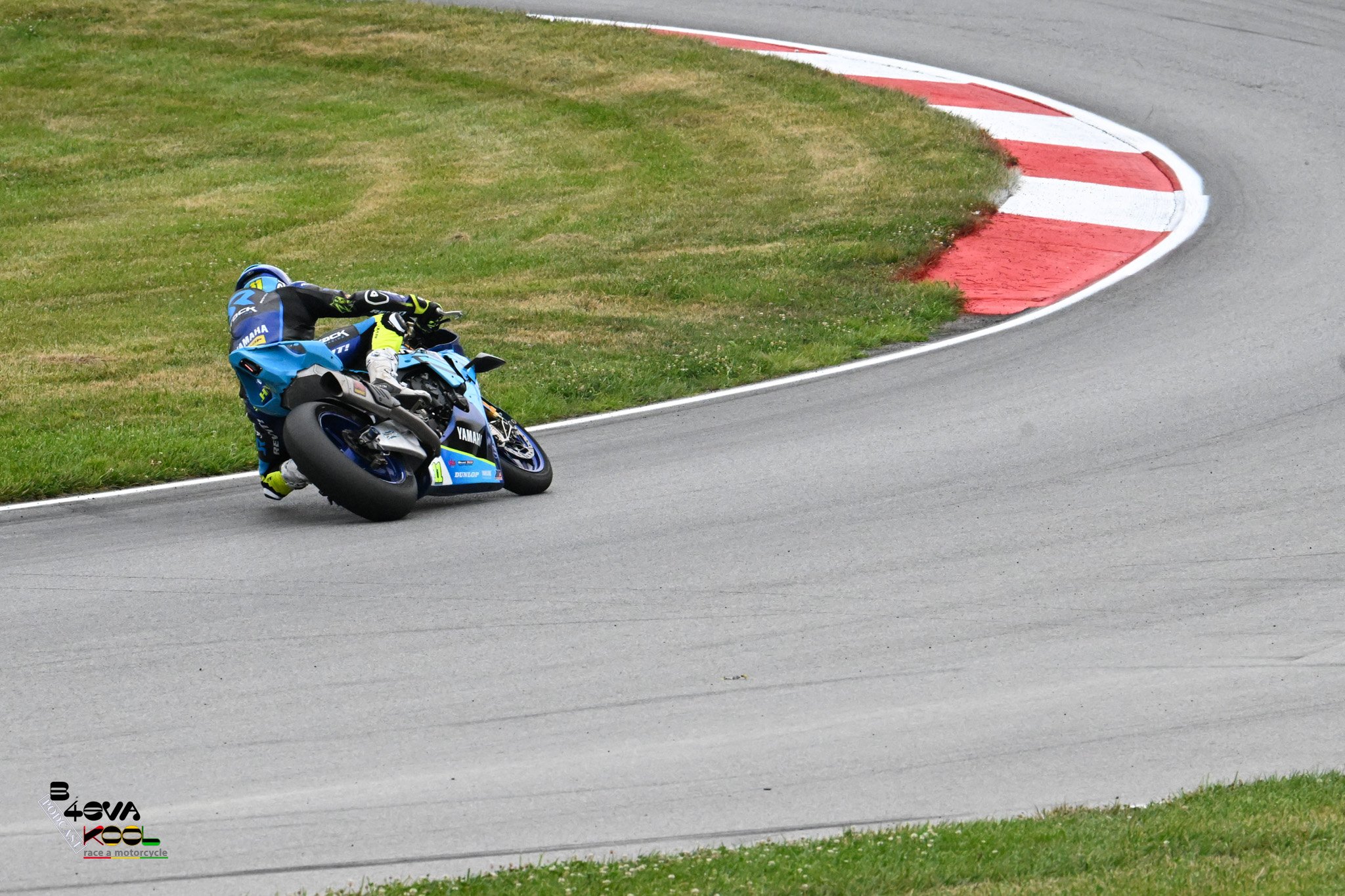 Motorsport rider in blue racing suit and helmet riding a blue Yamaha motorcycle on a racetrack, leaning into a curve on the track.