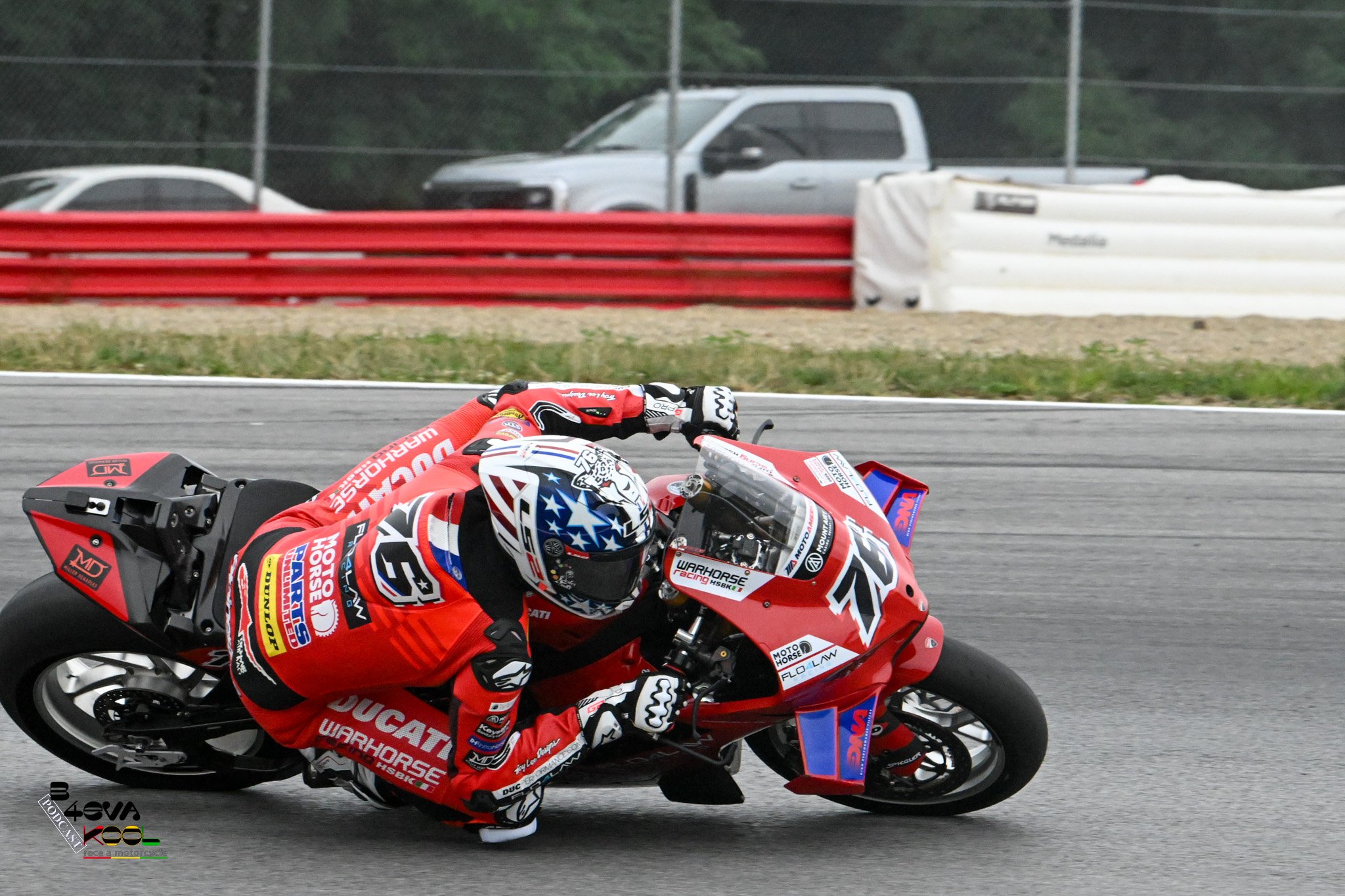 Motorsport race car rider in red racing gear leaning to the right on a red Ducati motorcycle on the race track.
