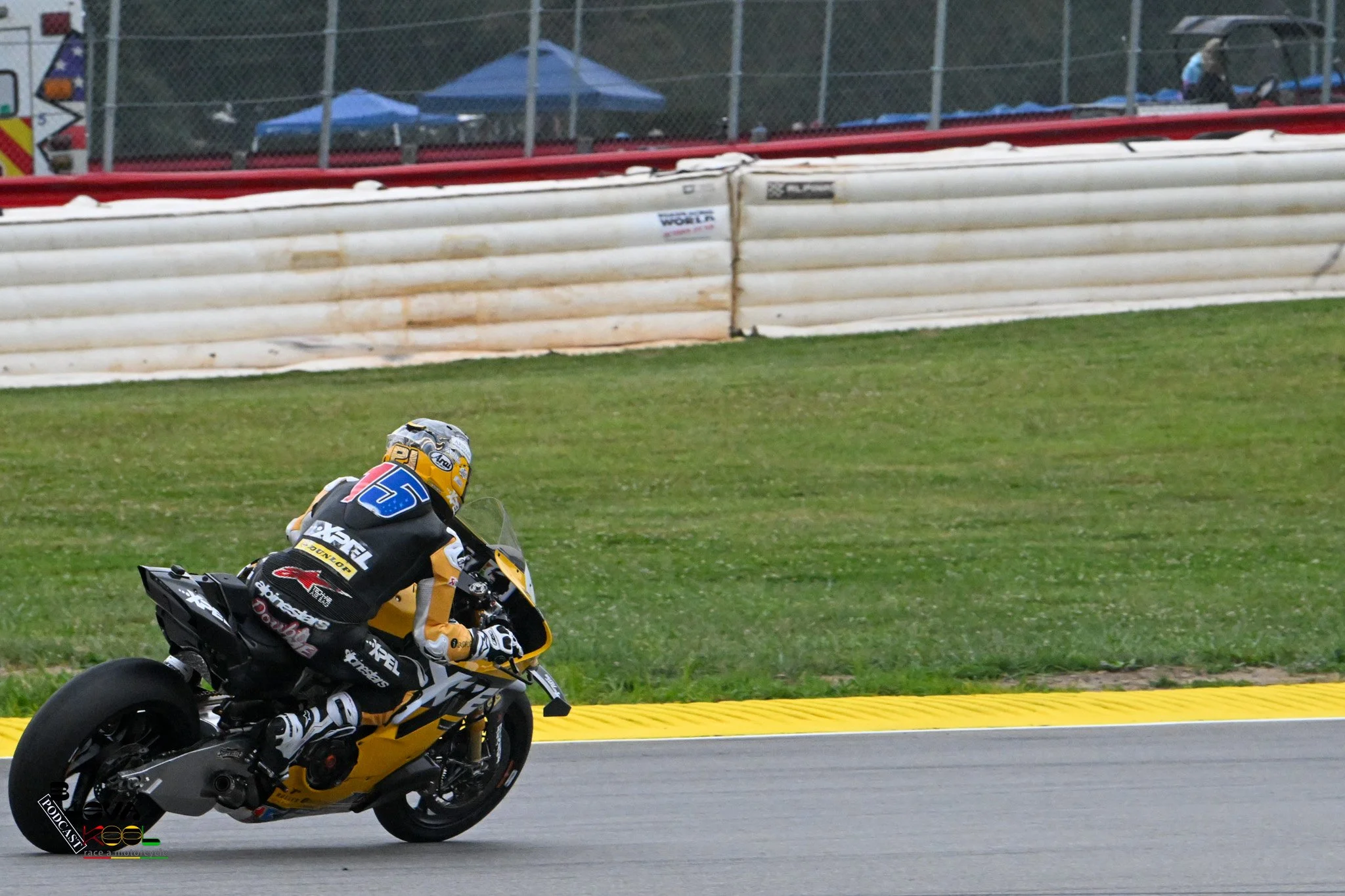 Motorcycle racer leaning into a turn during a race on a track with safety barriers and grass in the background.