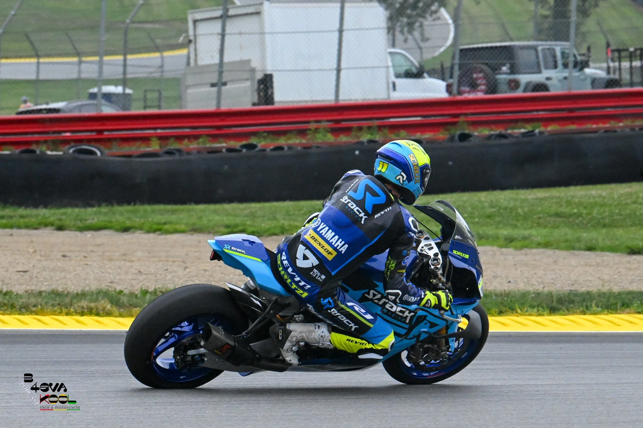 A motorcycle racer wearing a blue and yellow racing suit and helmet riding a blue Yamaha motorcycle on a race track.