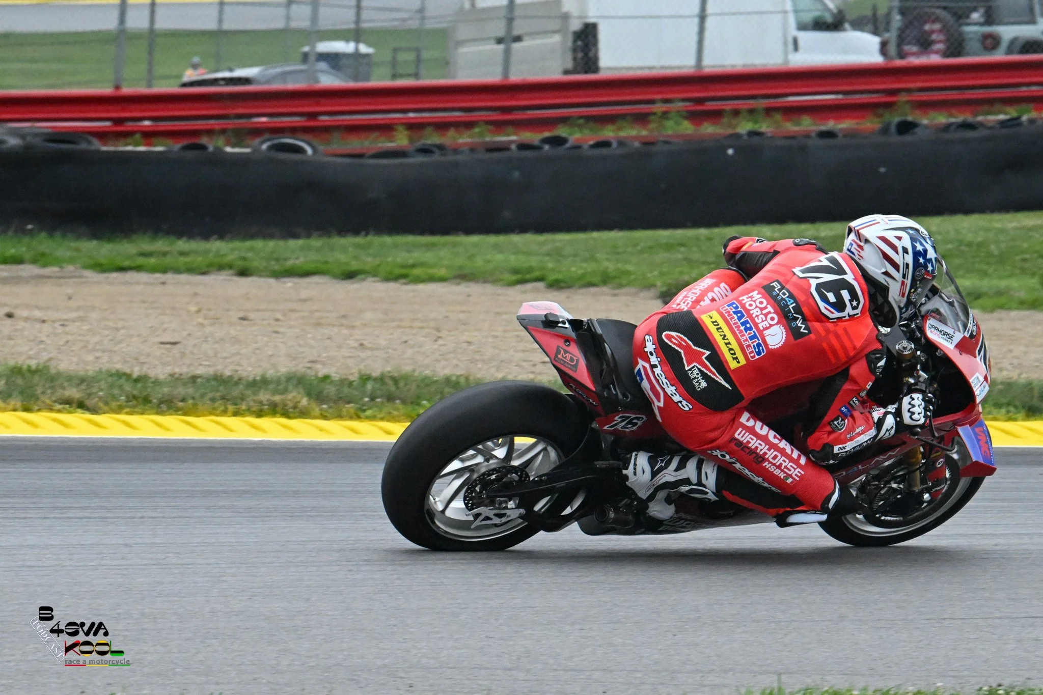 Motorcycle racer in red racing suit leaning into a turn on a race track.