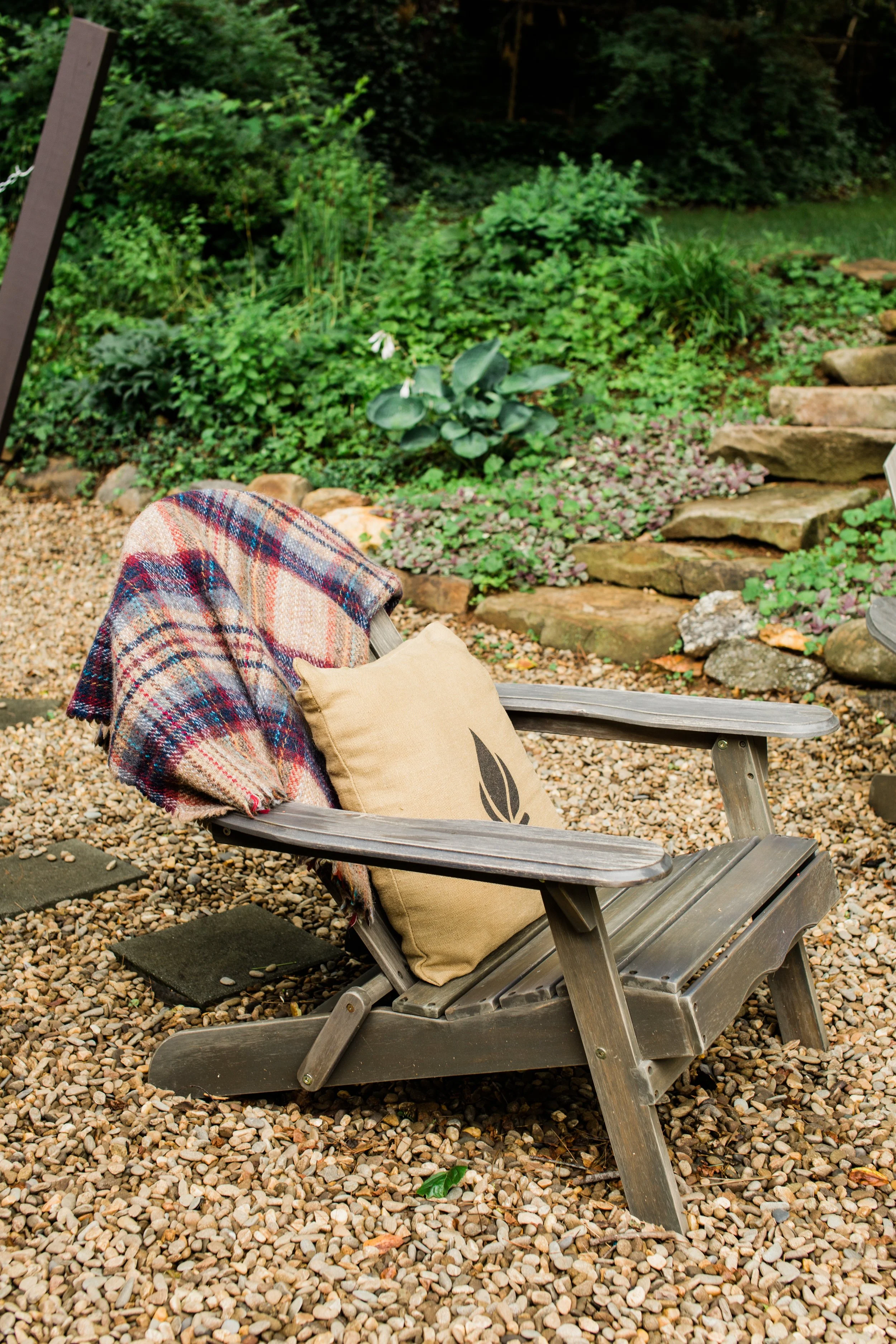 Plaid blanket on an Adirondack chair beside stone steps and a garden path.