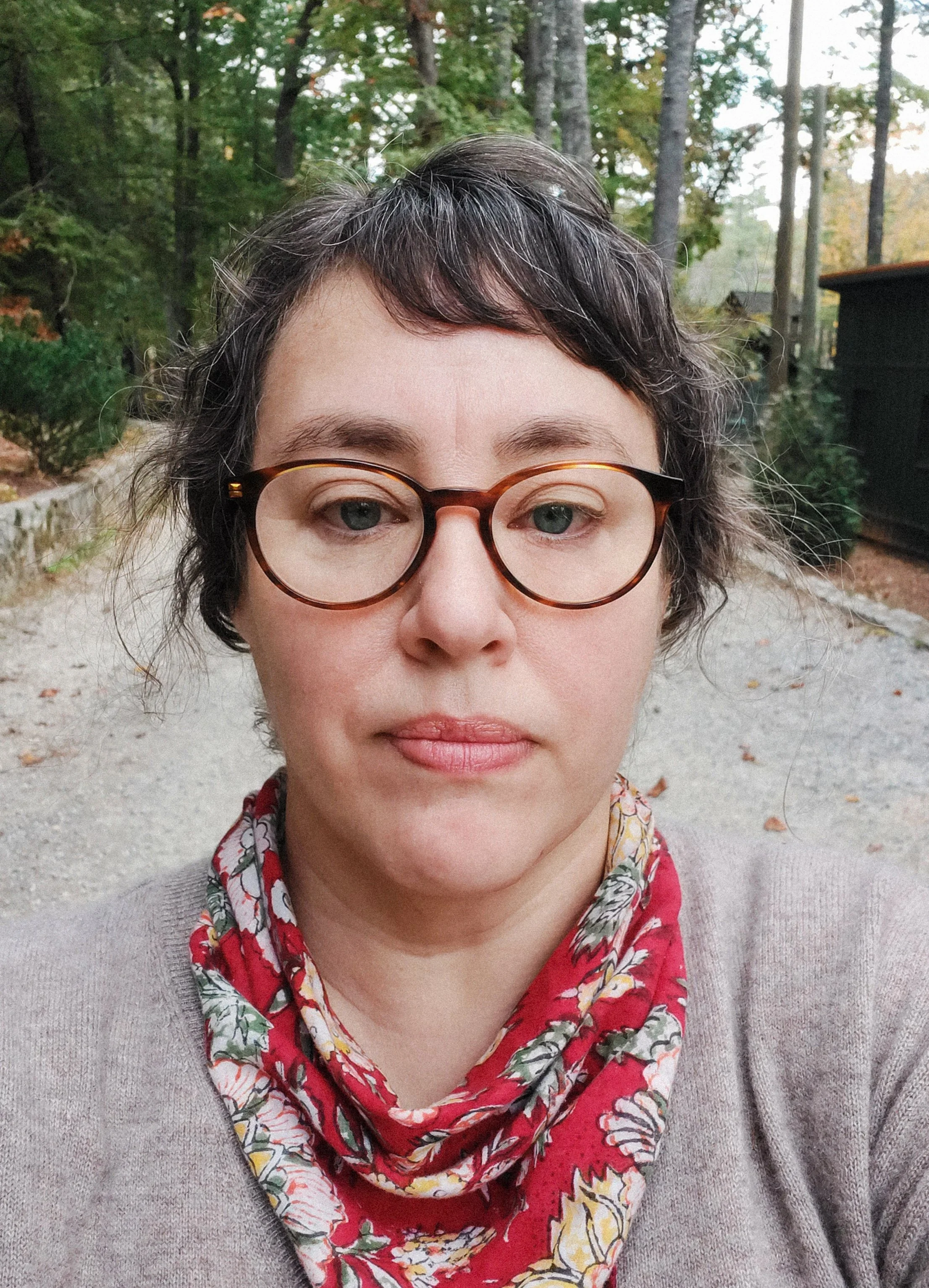 Photographer, Jennifer Callahan, in a red scarf and brown sweater on a wooded path.