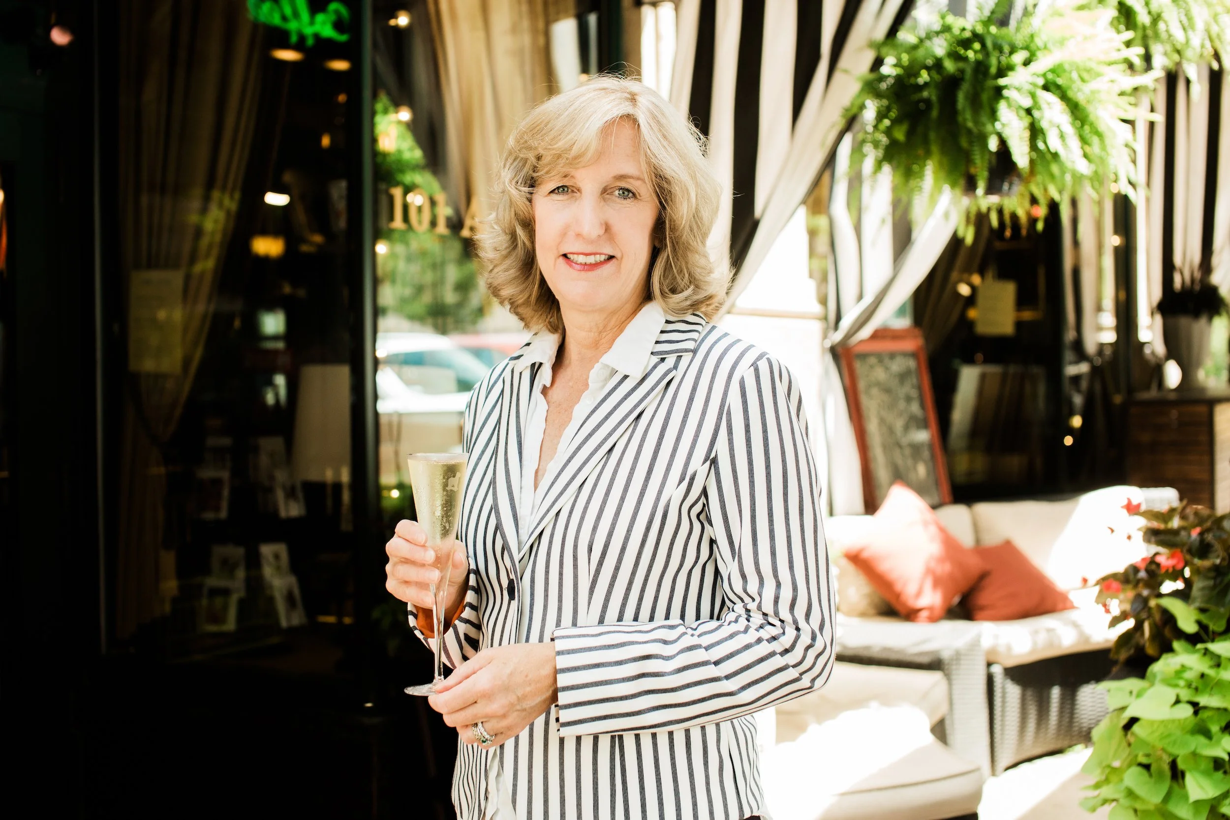 Donna Wright in a black and white striped blazer holding a champagne flute at the entrance to Battery Park Book Exchange in Asheville.