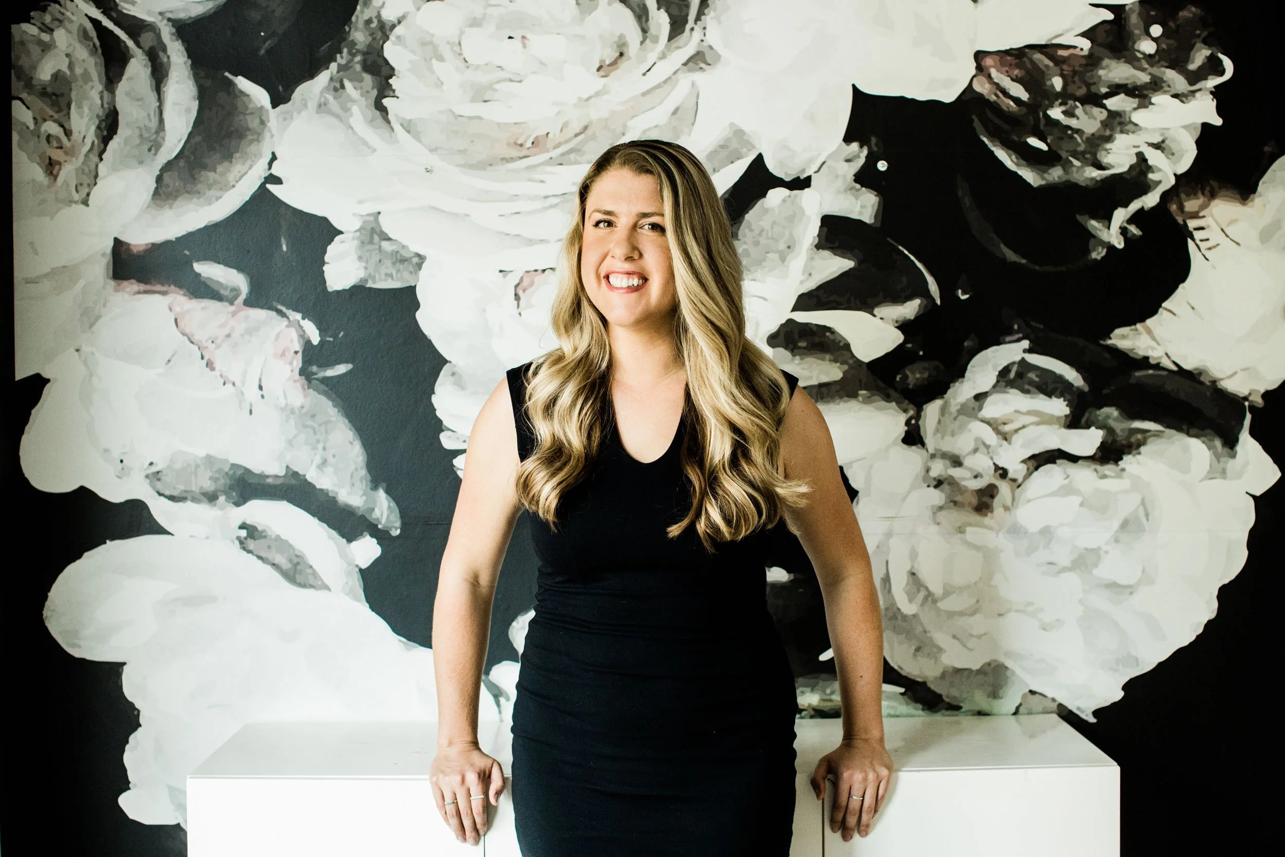 Event planner Erica Bastone smiles in front of bold black and white floral wallpaper.