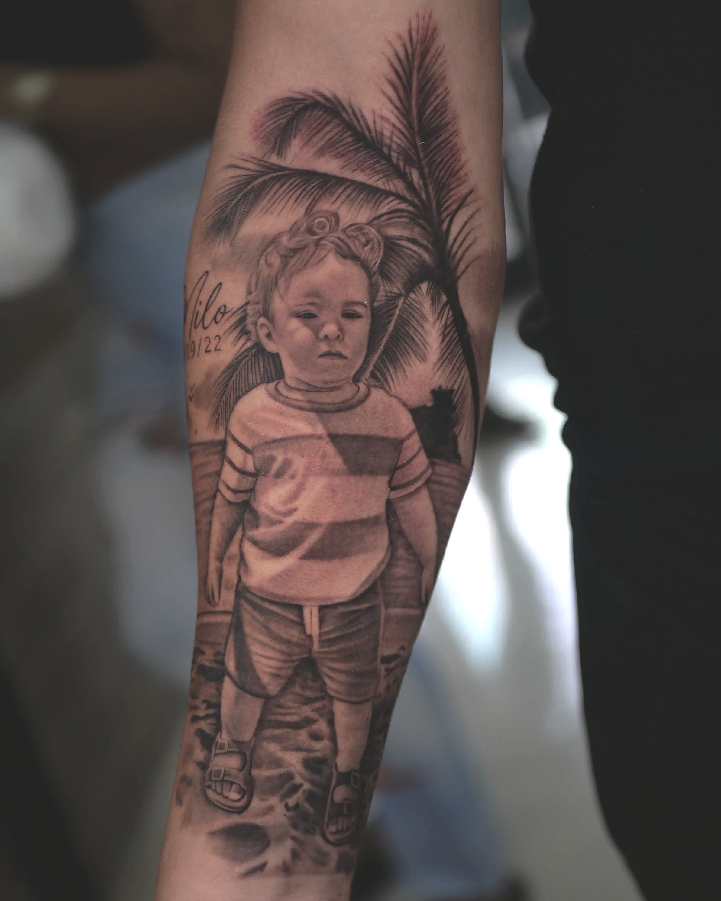 Tatuaje de un niño en el antebrazo con fondo de palma, perfil y nombre 'Milo'