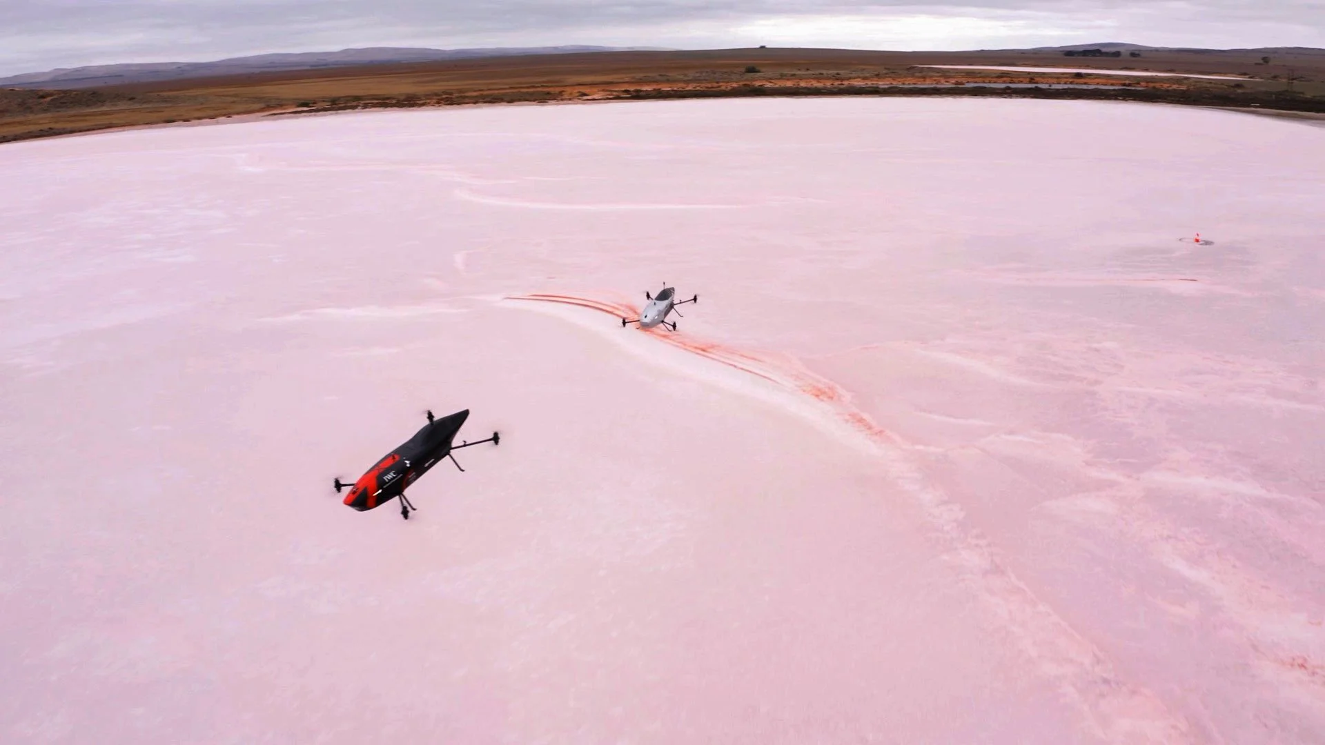 Two speeders flying-racing over a pink salt flat.