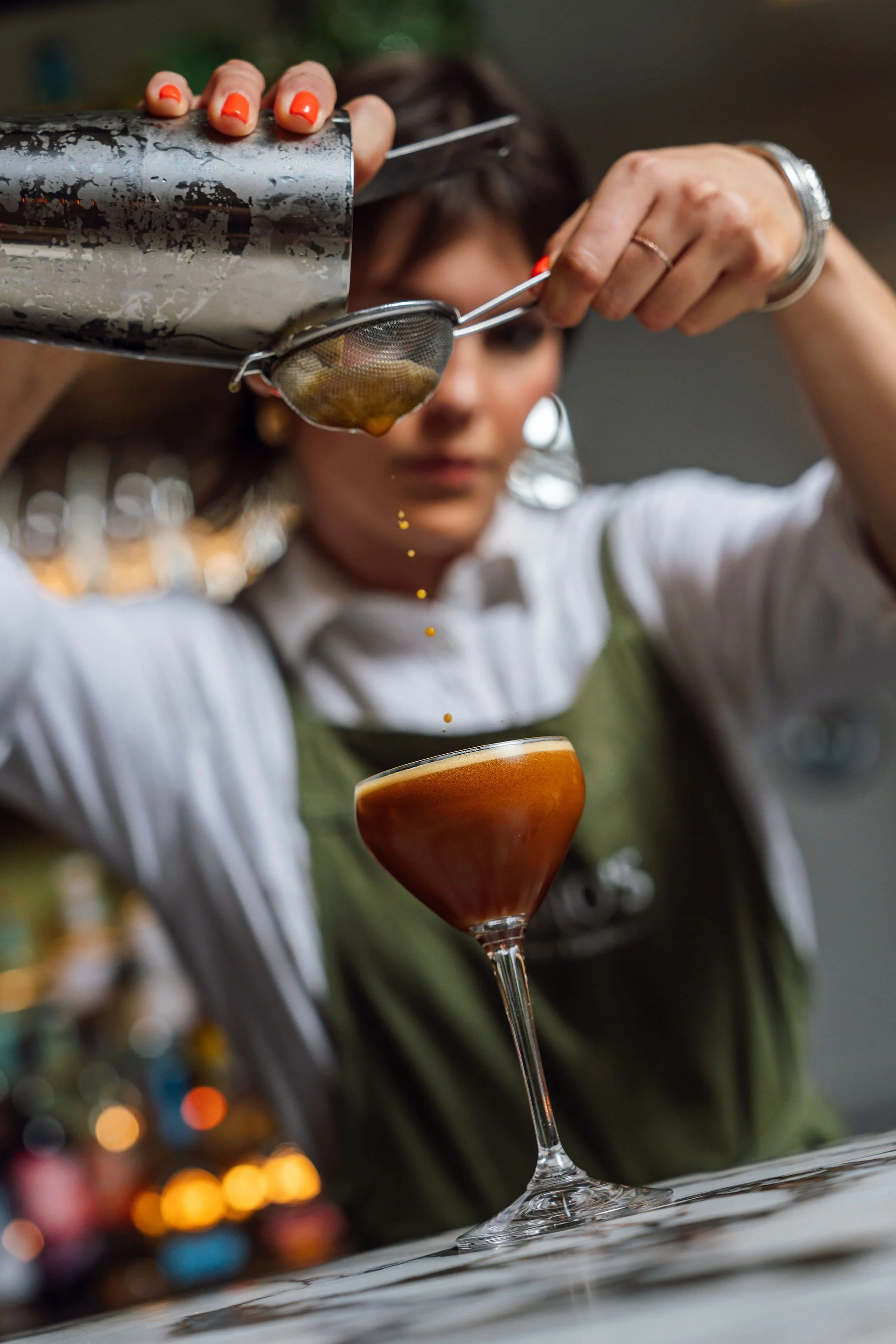 A bartender pours a layered cocktail into a glass through a strainer.