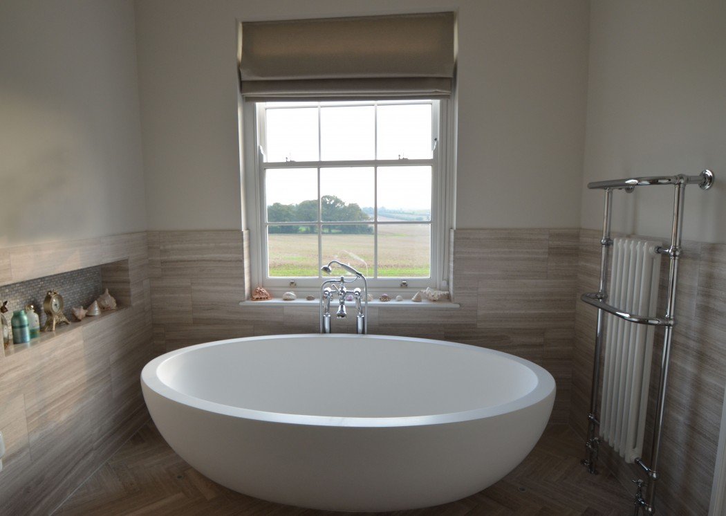 A modern bathroom with a freestanding oval bathtub, a window with a countryside view, decorative items on the windowsill, and a heated towel rack.