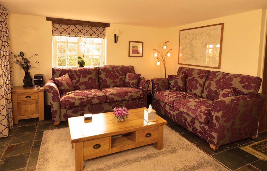 Cozy living room with two purple floral sofas, wooden coffee table, floor lamp, and wall art.
