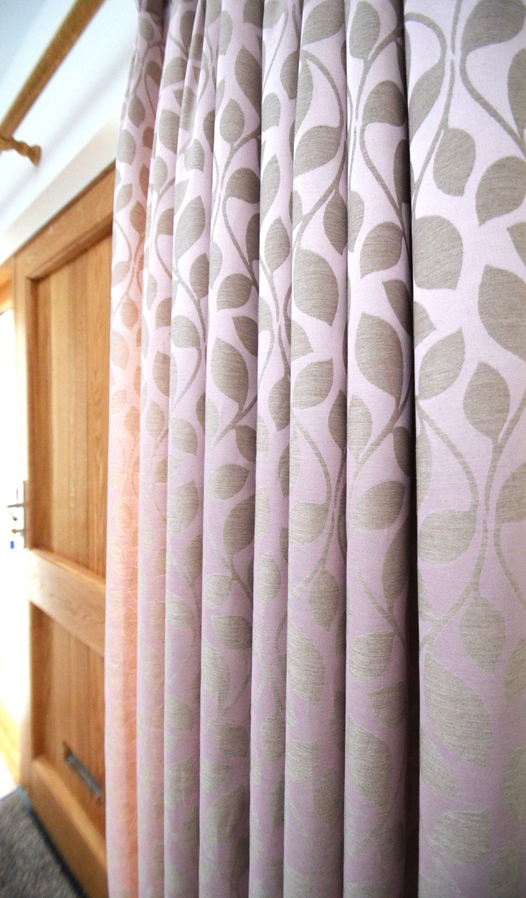 Pink curtains with a leaf pattern hanging next to a wooden door.