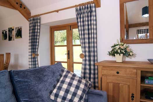 Cozy living room with blue and white checkered curtains, a matching pillow on a velvet sofa, a wooden sideboard with flowers, and a mirror above.