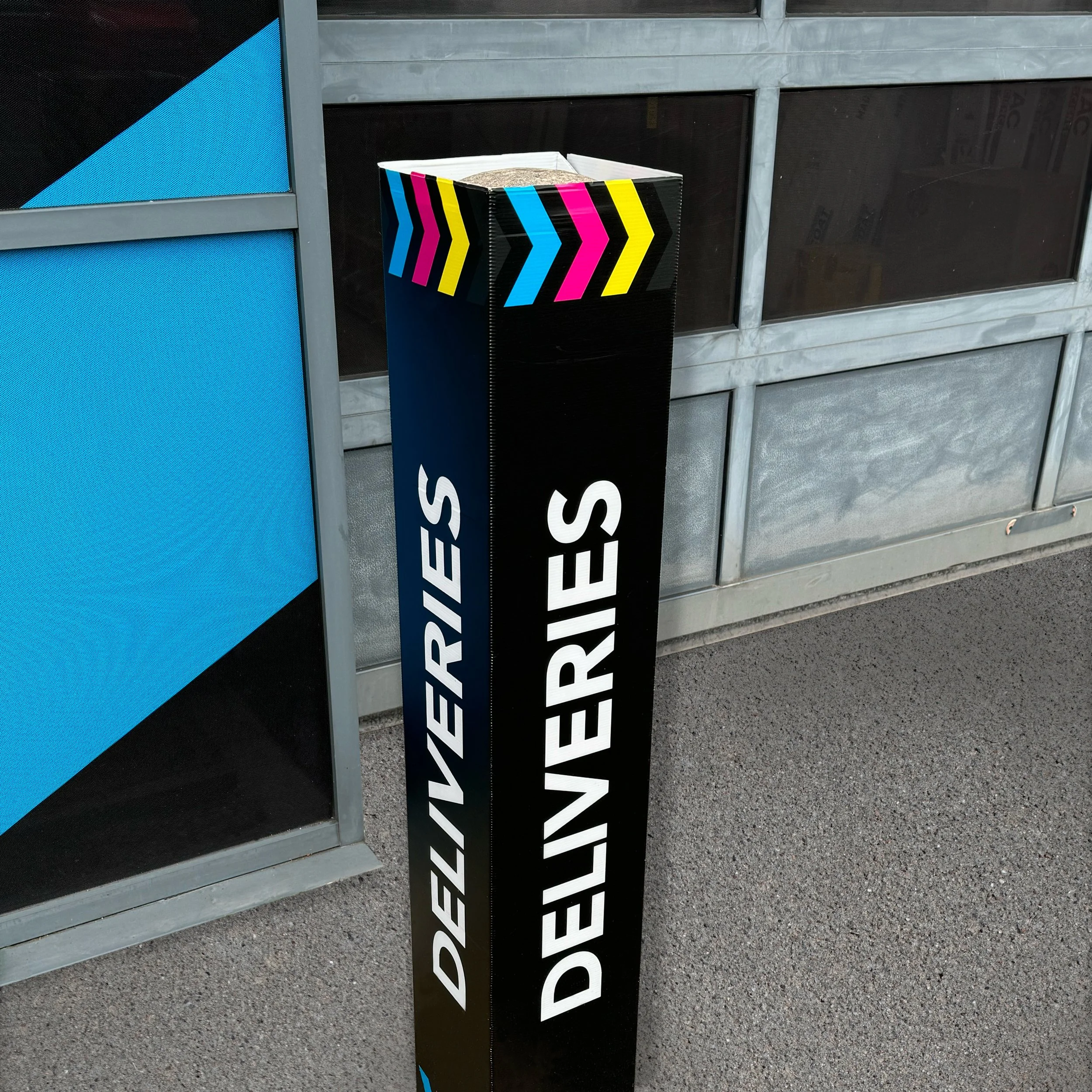 Correx bollard cover labelled 'Deliveries' with colorful arrows outside a shutter door