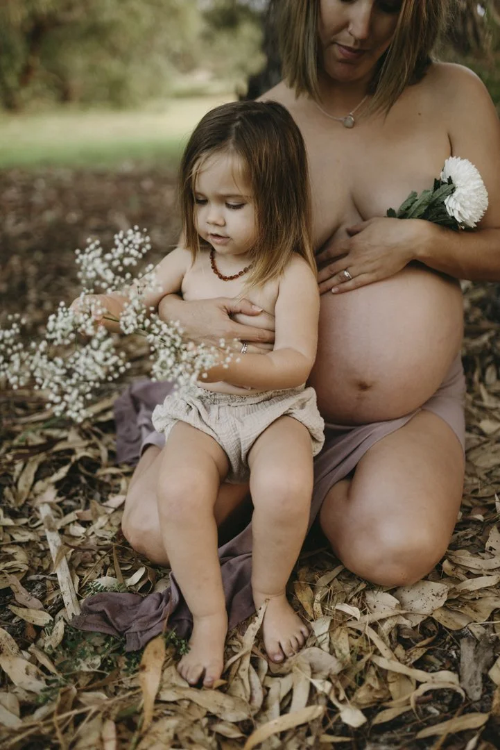 Pregnant woman holding child with flowers in outdoor setting