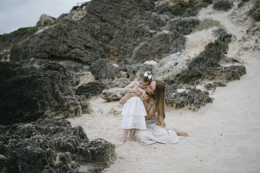 A woman and child hugging on a rocky beach.