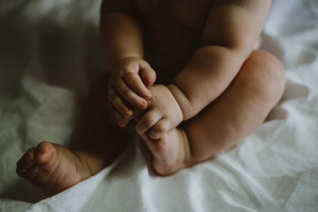 Close-up of a baby's hands and legs on white fabric.