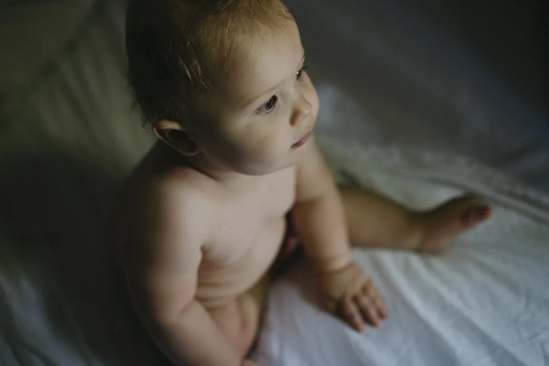 Baby sitting on a bed, looking upward, with a soft lighting.