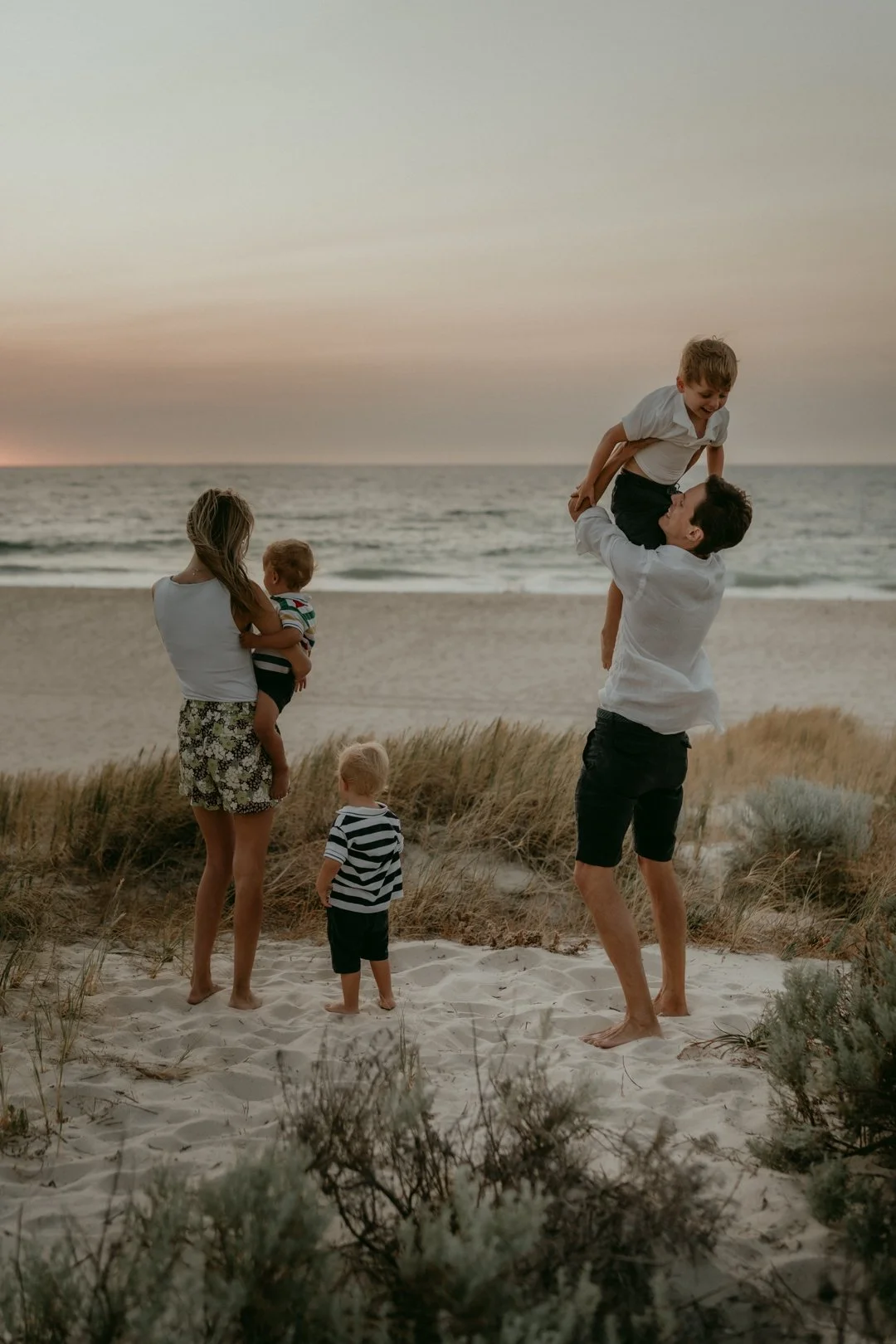 Family playing on a sandy beach during sunset, with two adults and two children, near the ocean.