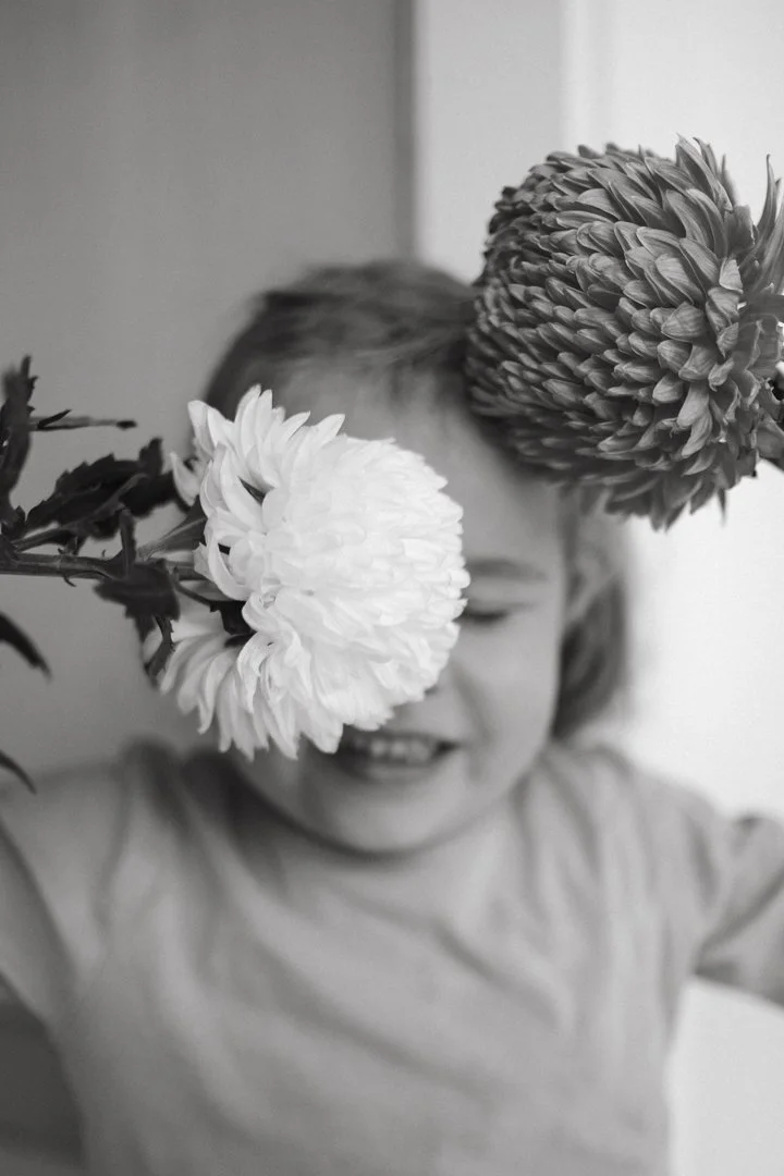 Black and white photo of a child smiling with flowers obscuring their face.