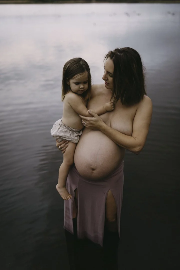 Pregnant woman holding child in water.