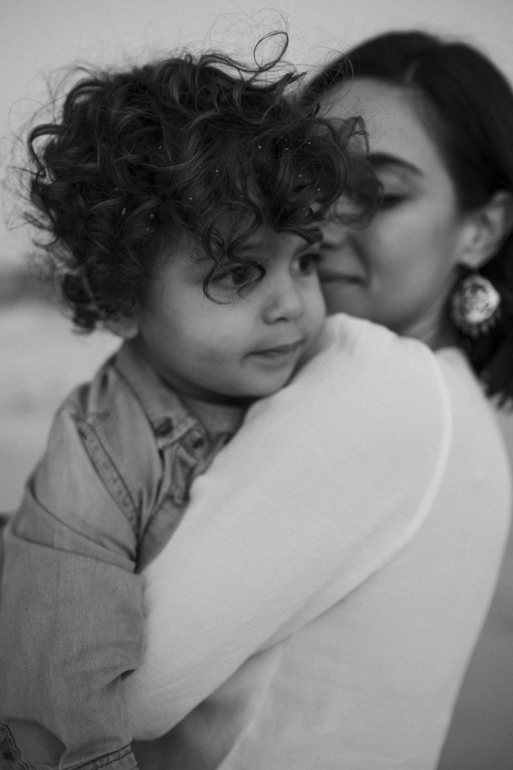 Black and white photo of a woman holding a young child, both with curly hair, in an affectionate embrace.