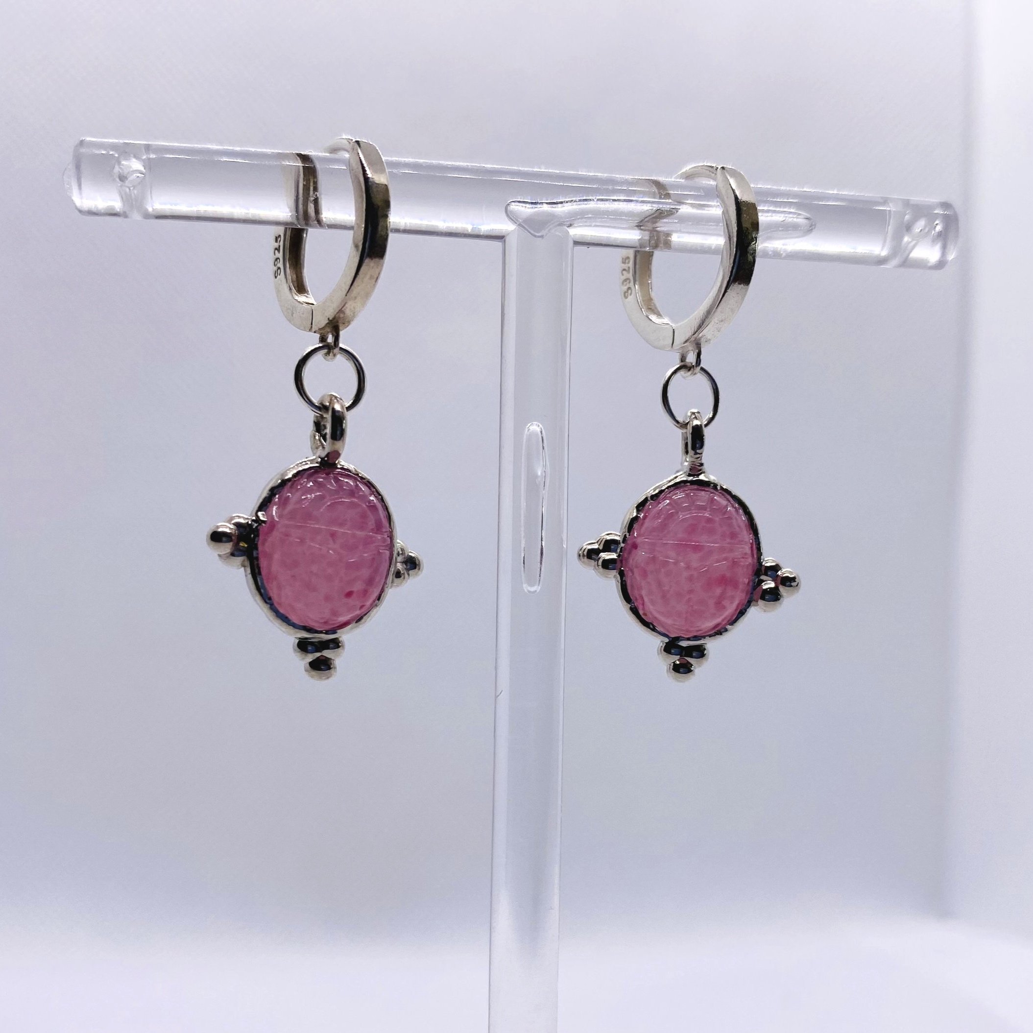 A one-of-a-kind pair of vintage earrings inspired by Egyptian Revival, featuring rare 1940s orchid pink scarabs, set in palladium-plated bezels with sterling silver huggie hoops.