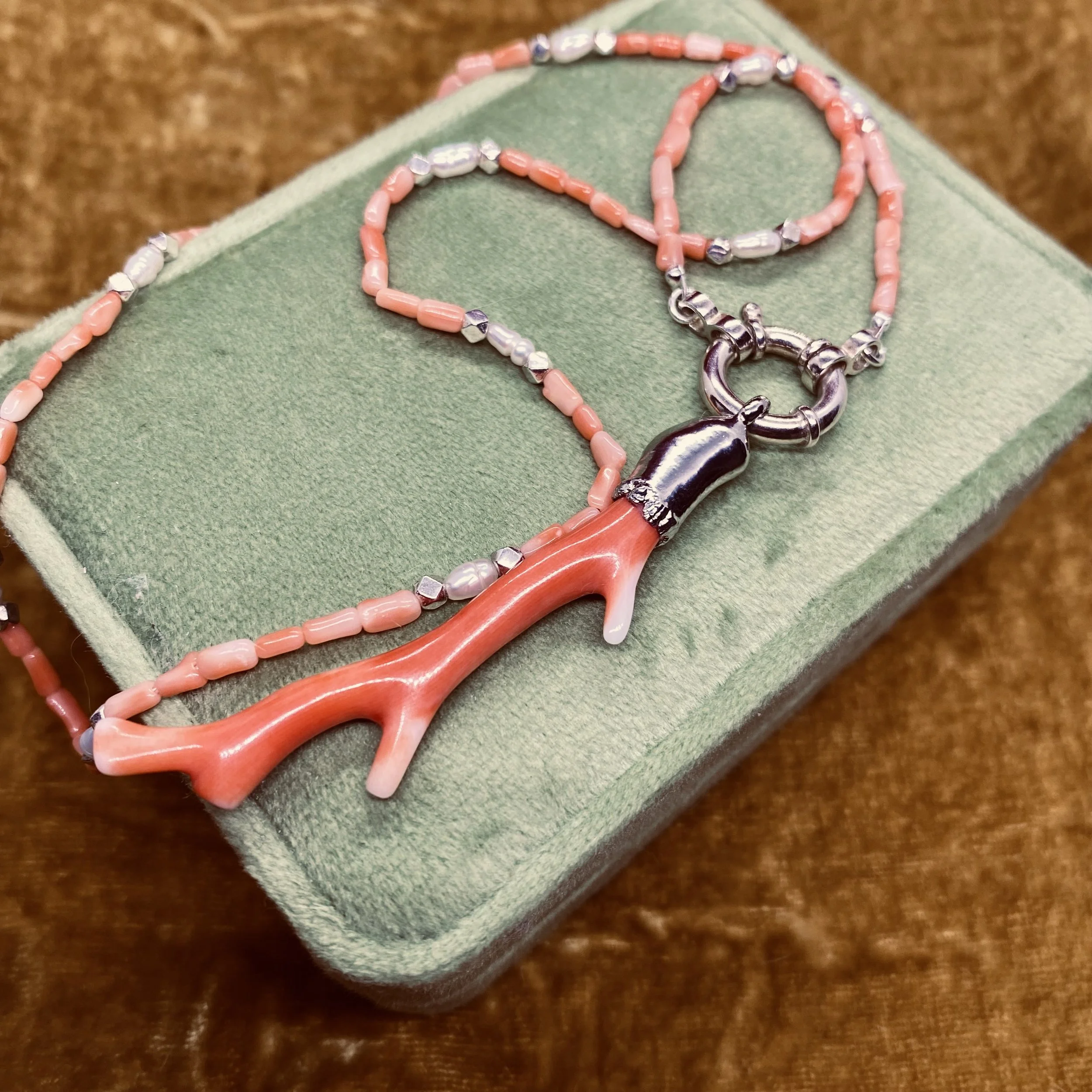 flat lay of coralie necklace on green velvet box with pink velvet backdrop