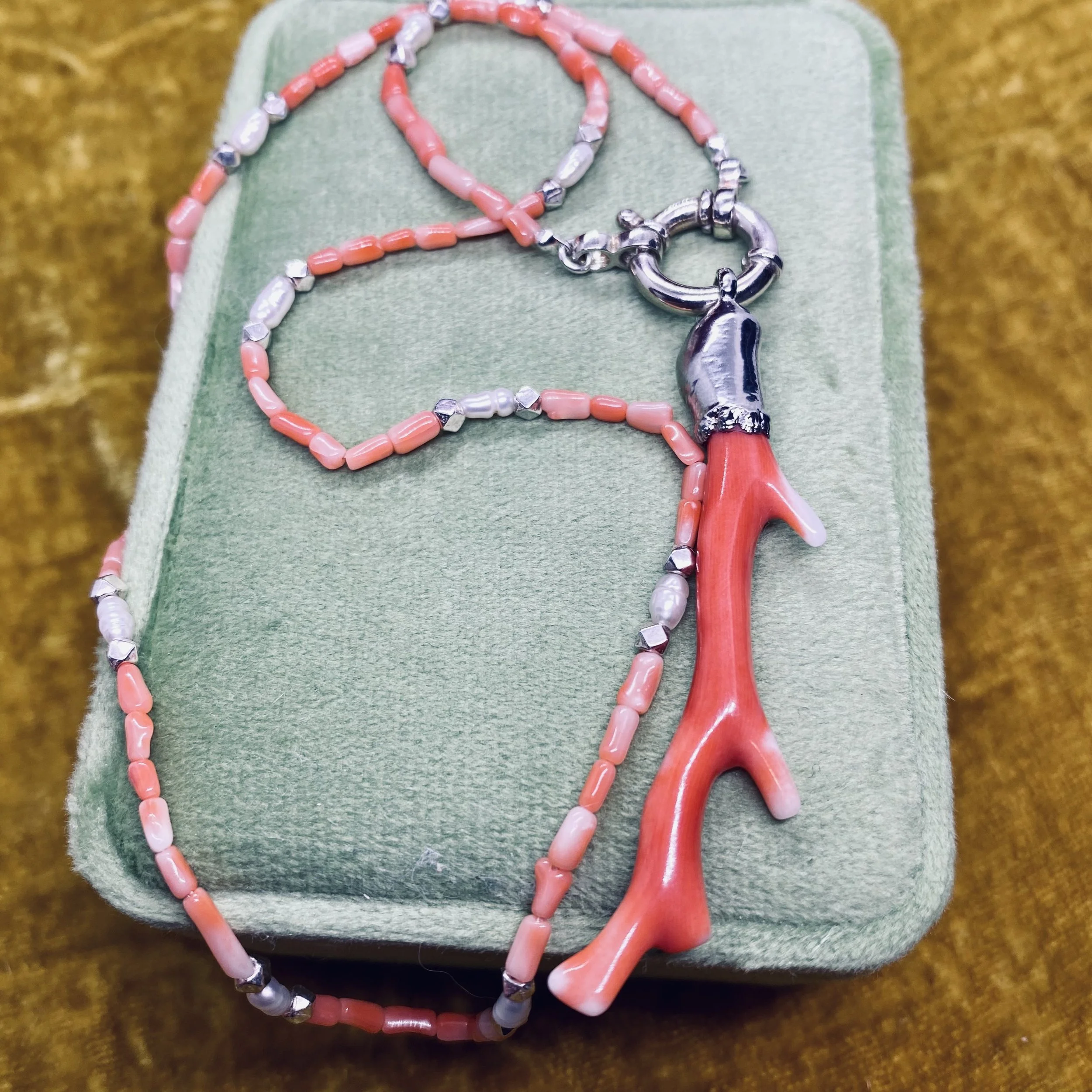 flat lay of coralie necklace on green velvet box with pink velvet backdrop