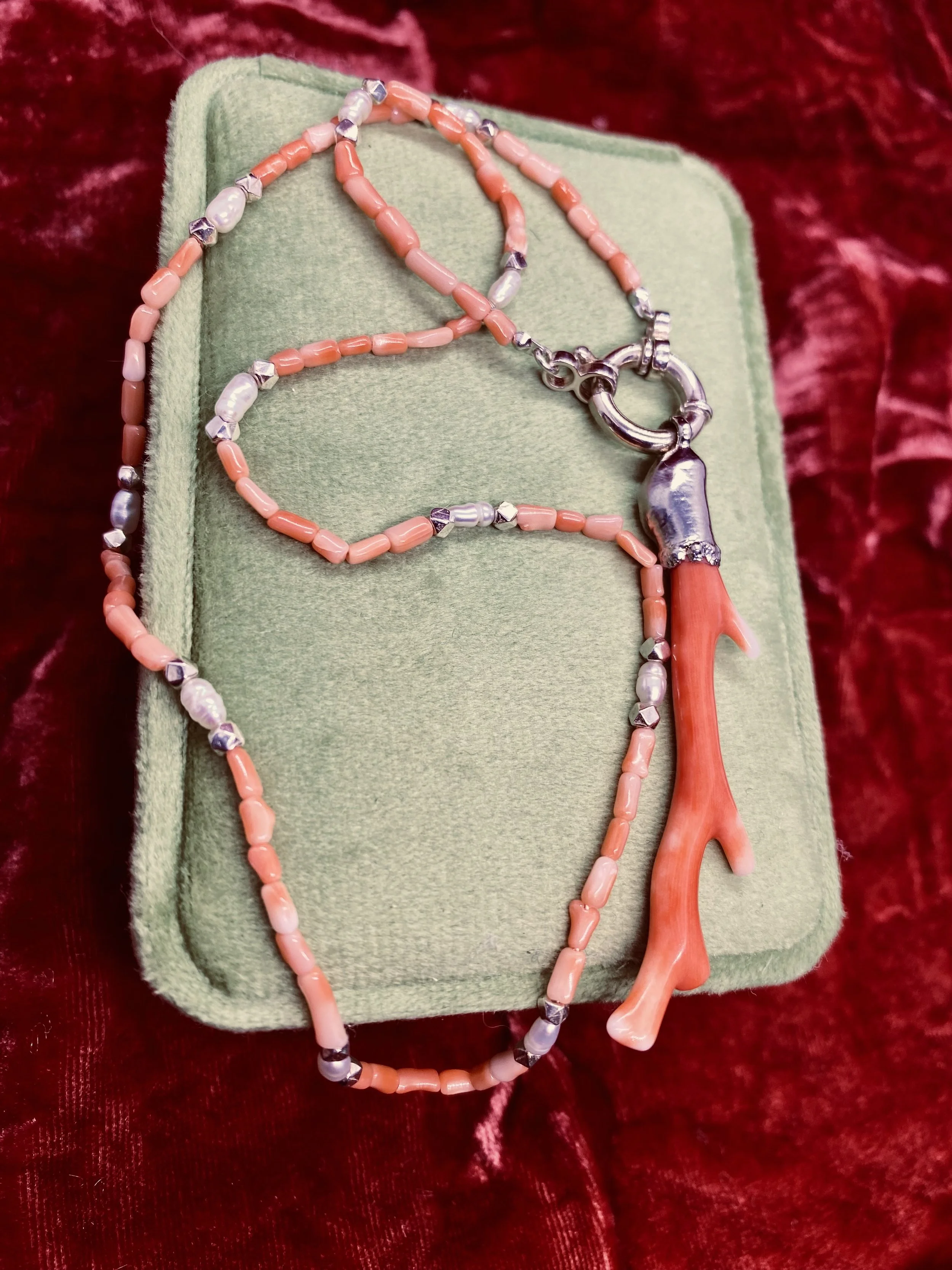 coralie necklace draped on a green velvet box with pink velvet backdrop