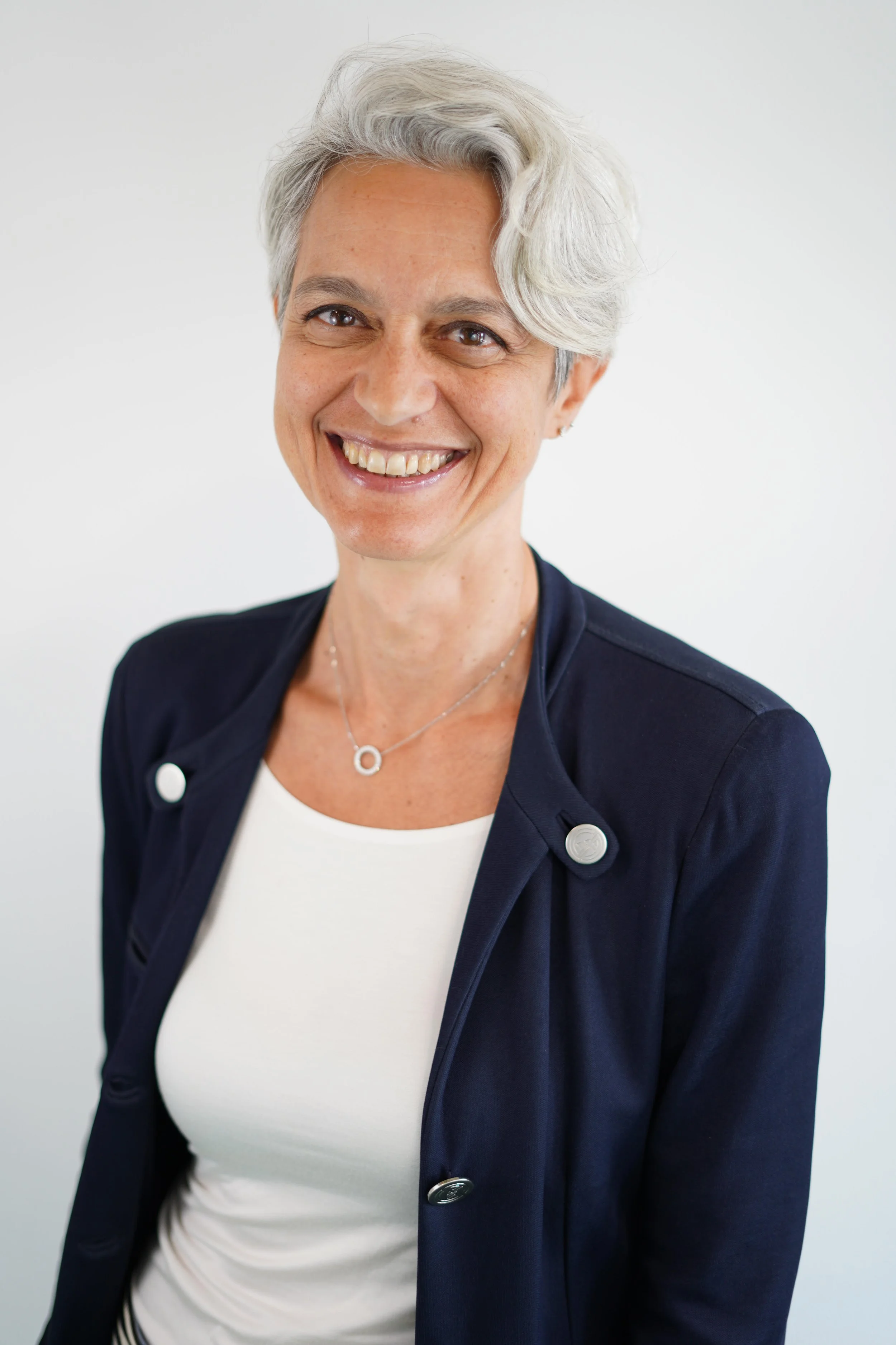 Close-up portrait of a woman with short gray hair, smiling and wearing a dark blazer.