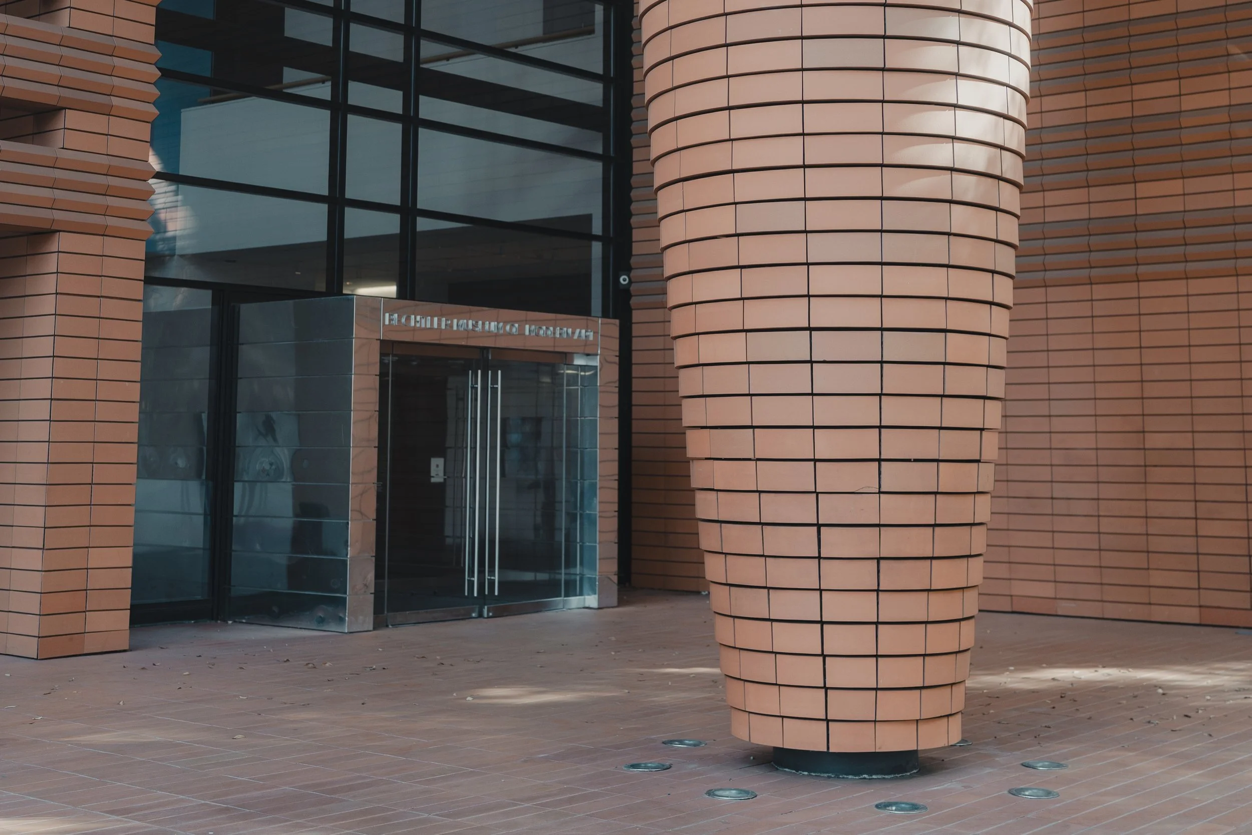 Architectural detail of a large, textured pillar next to a sleek glass entrance, providing a clean, contemporary setting for fashion and lifestyle shots.