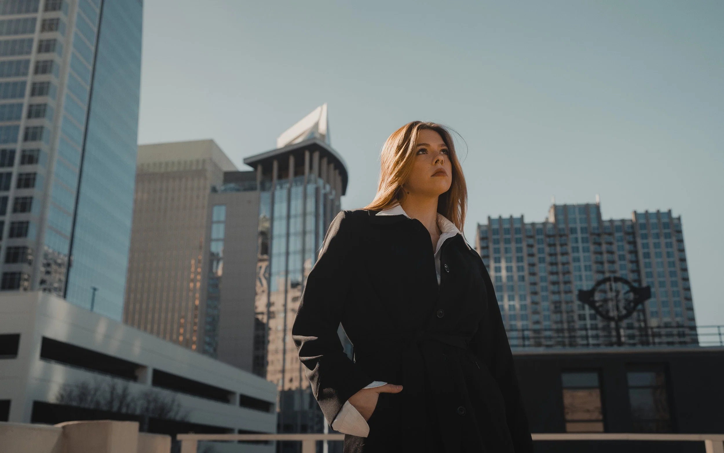 Woman in black coat stands against Charlotte city skyline.