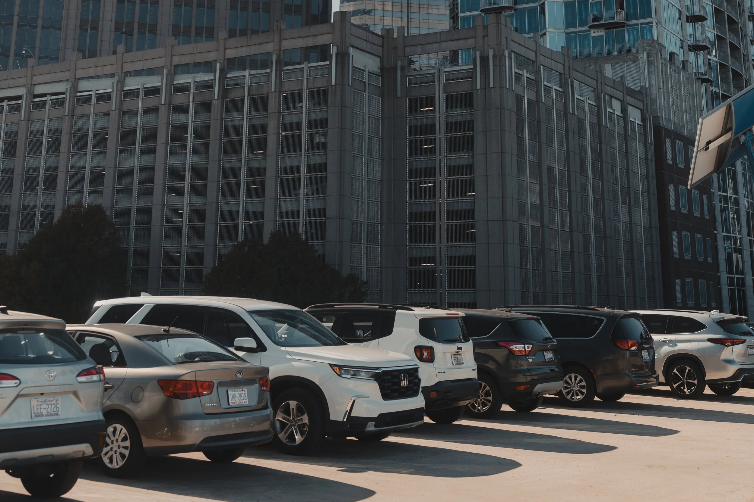 A line of modern vehicles parked in an urban environment with a large, textured high-rise building behind, suggesting movement and a high-end lifestyle context.