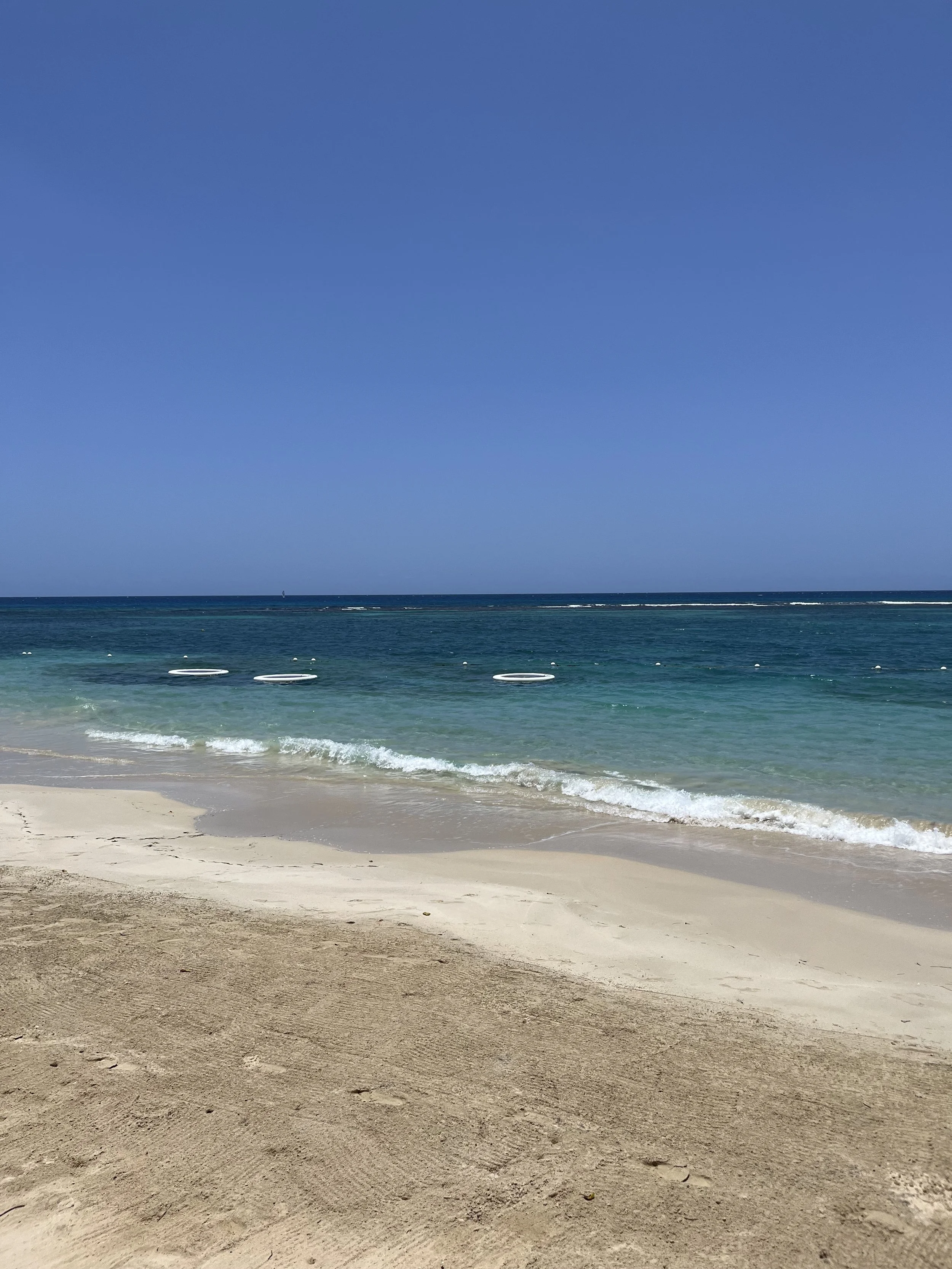 A sandy beach with small waves rolling onto the shore and a clear blue sky overhead.