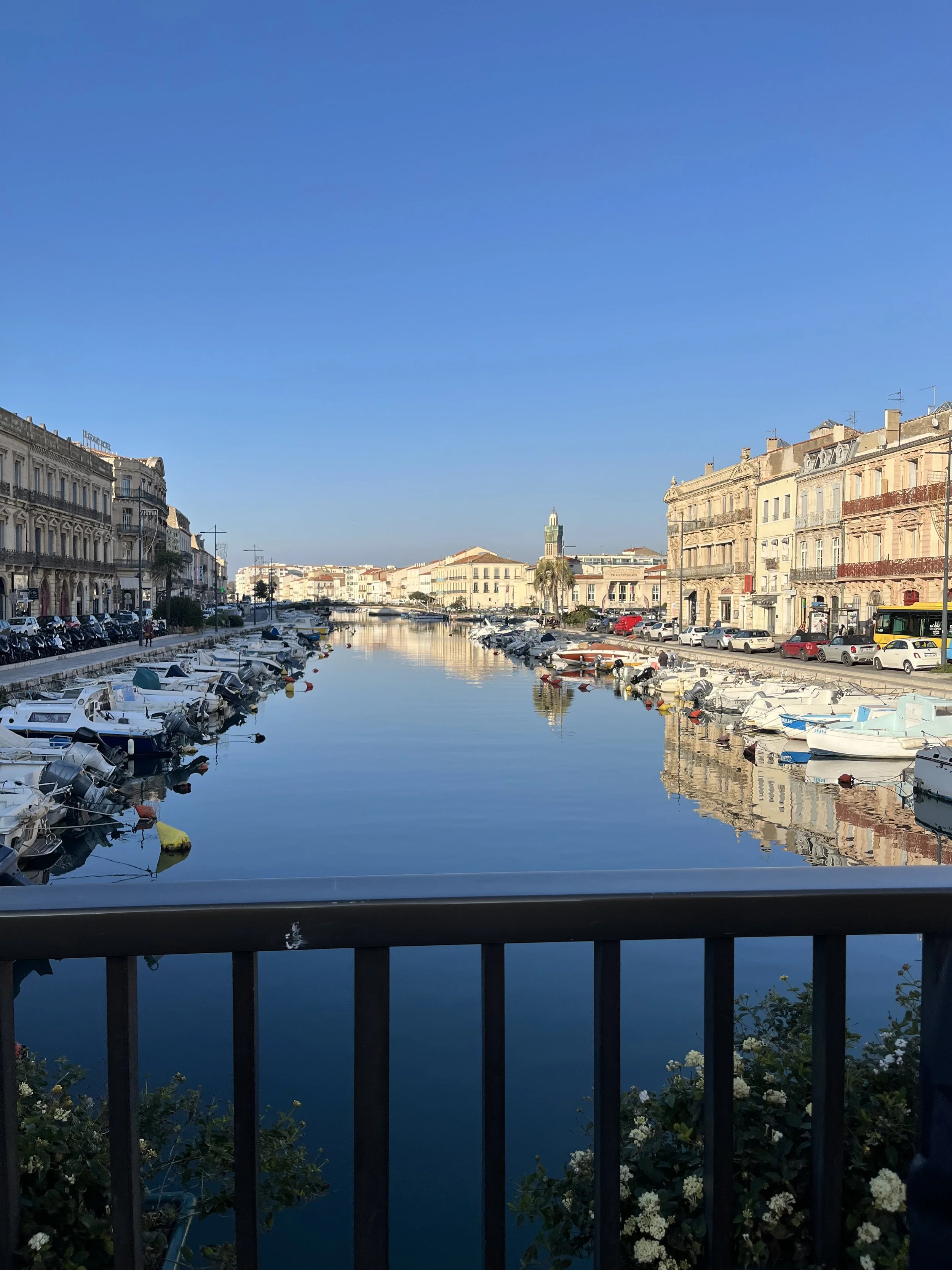 A view of a harbor with boats docked along the water, lined with historic buildings, under a clear blue sky.